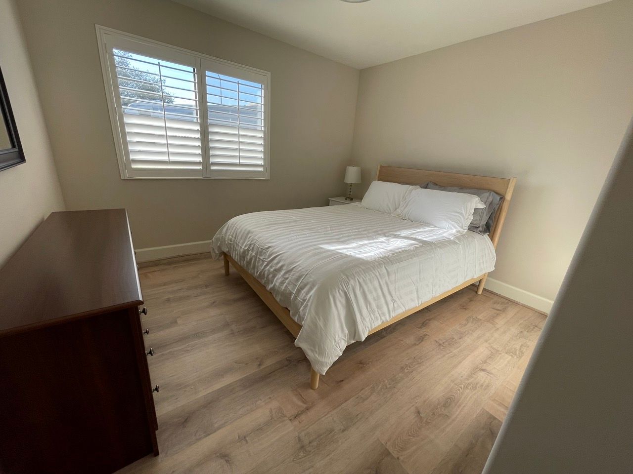 A bedroom with a bed , dresser and window with shutters.