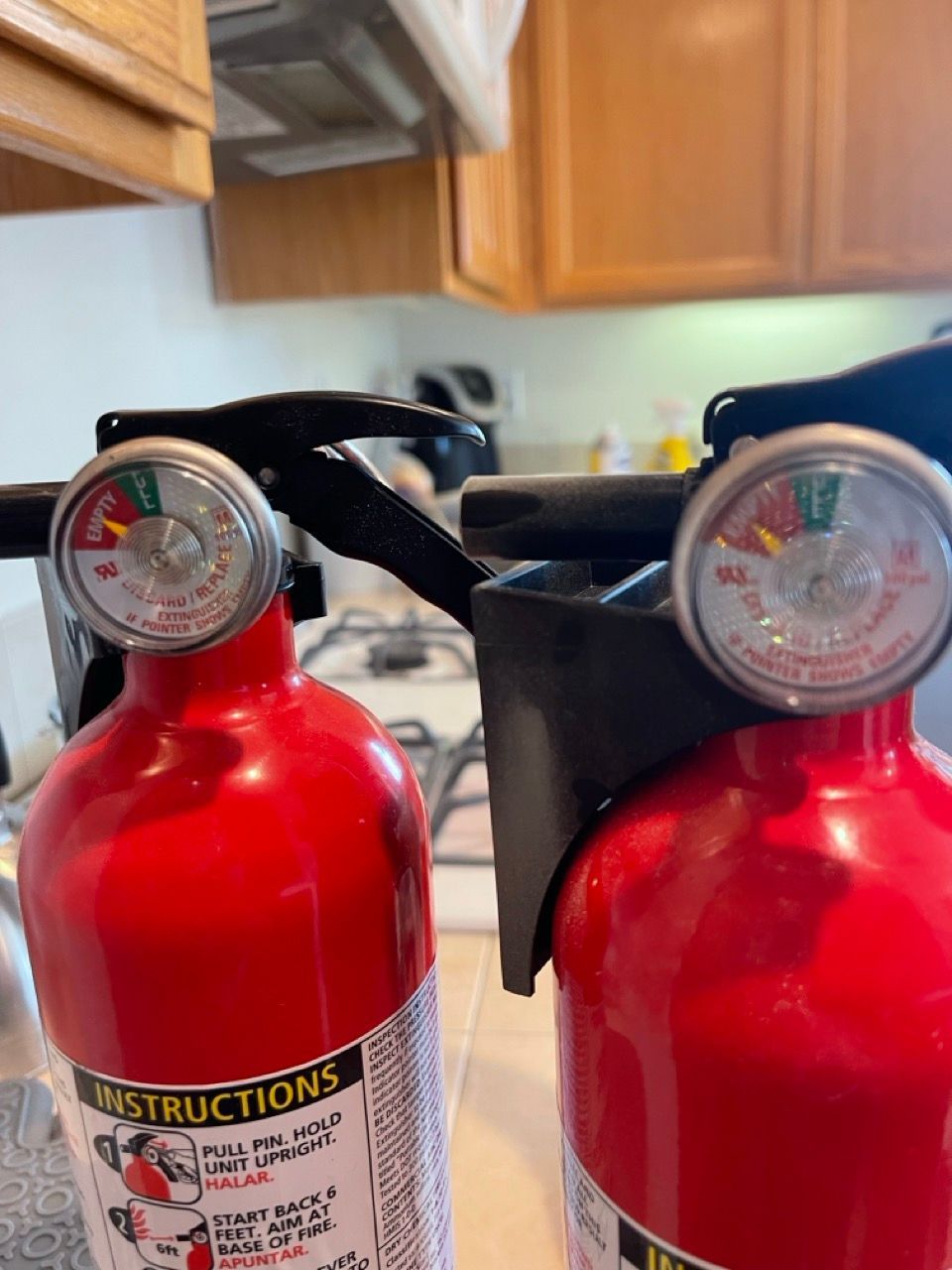 Two red fire extinguishers are sitting on a counter in a kitchen.