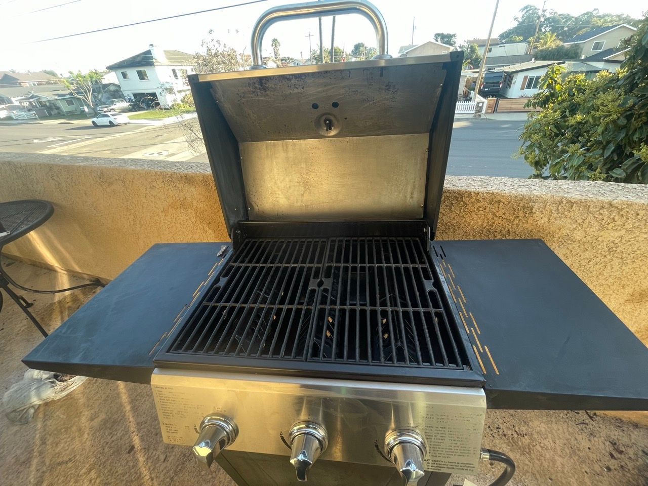 A grill with the lid open is sitting on a balcony