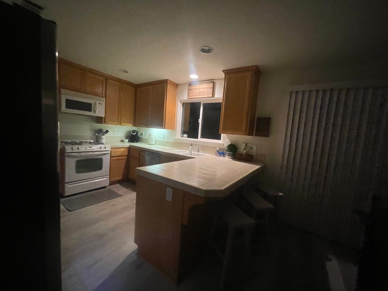 A kitchen with a stove , refrigerator , microwave , sink and window.