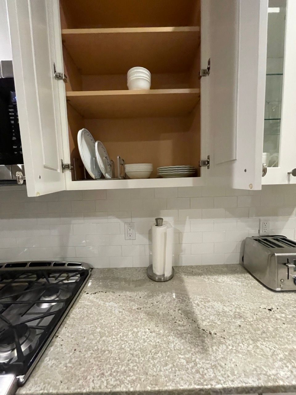 A kitchen with a stove , a toaster oven , and a cabinet filled with plates and bowls.