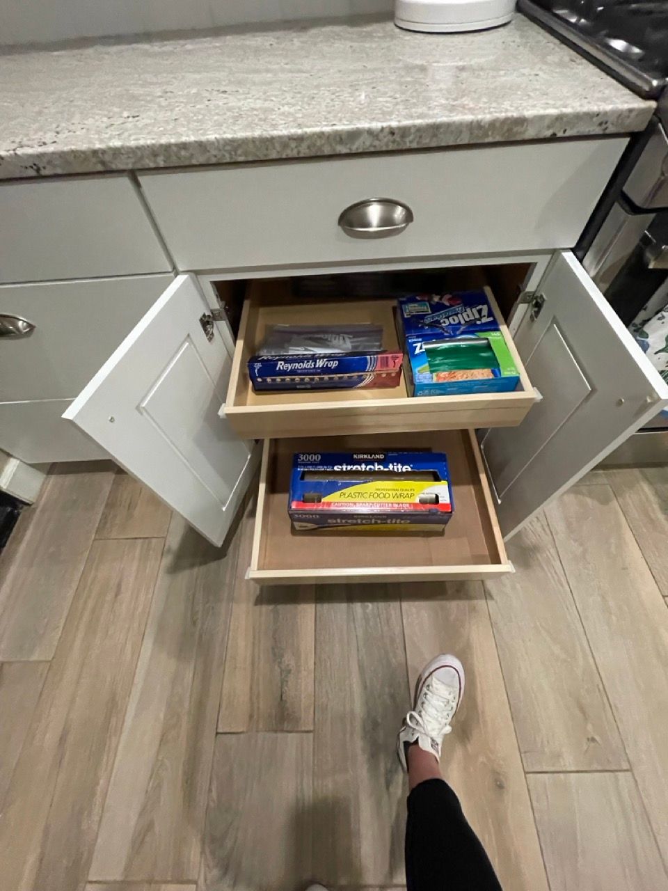 A person is standing in front of a kitchen drawer filled with food.
