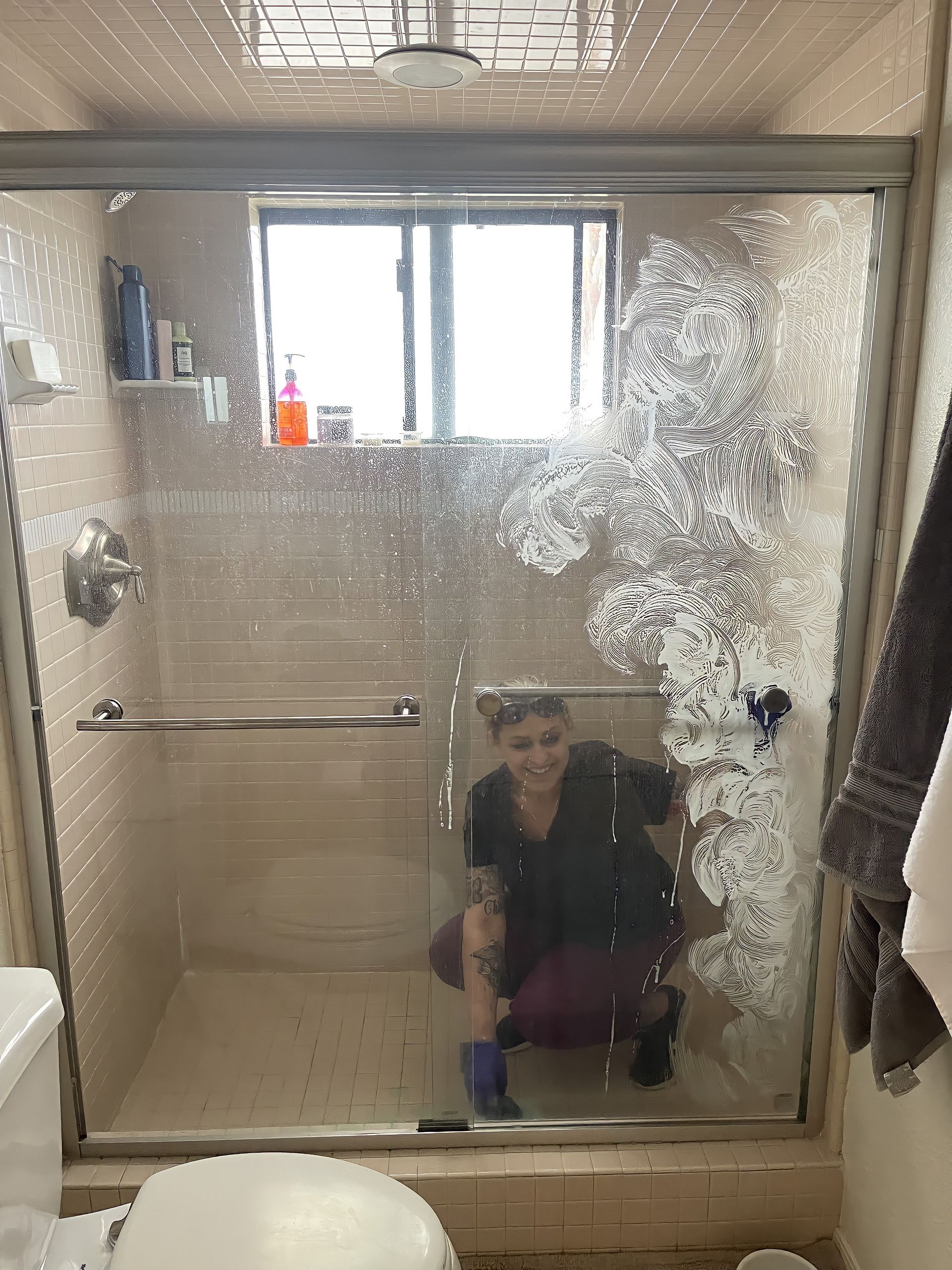 A woman is cleaning a shower door in a bathroom.