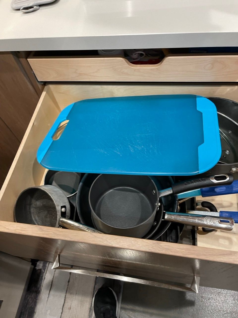 A kitchen drawer filled with pots and pans and a blue cutting board