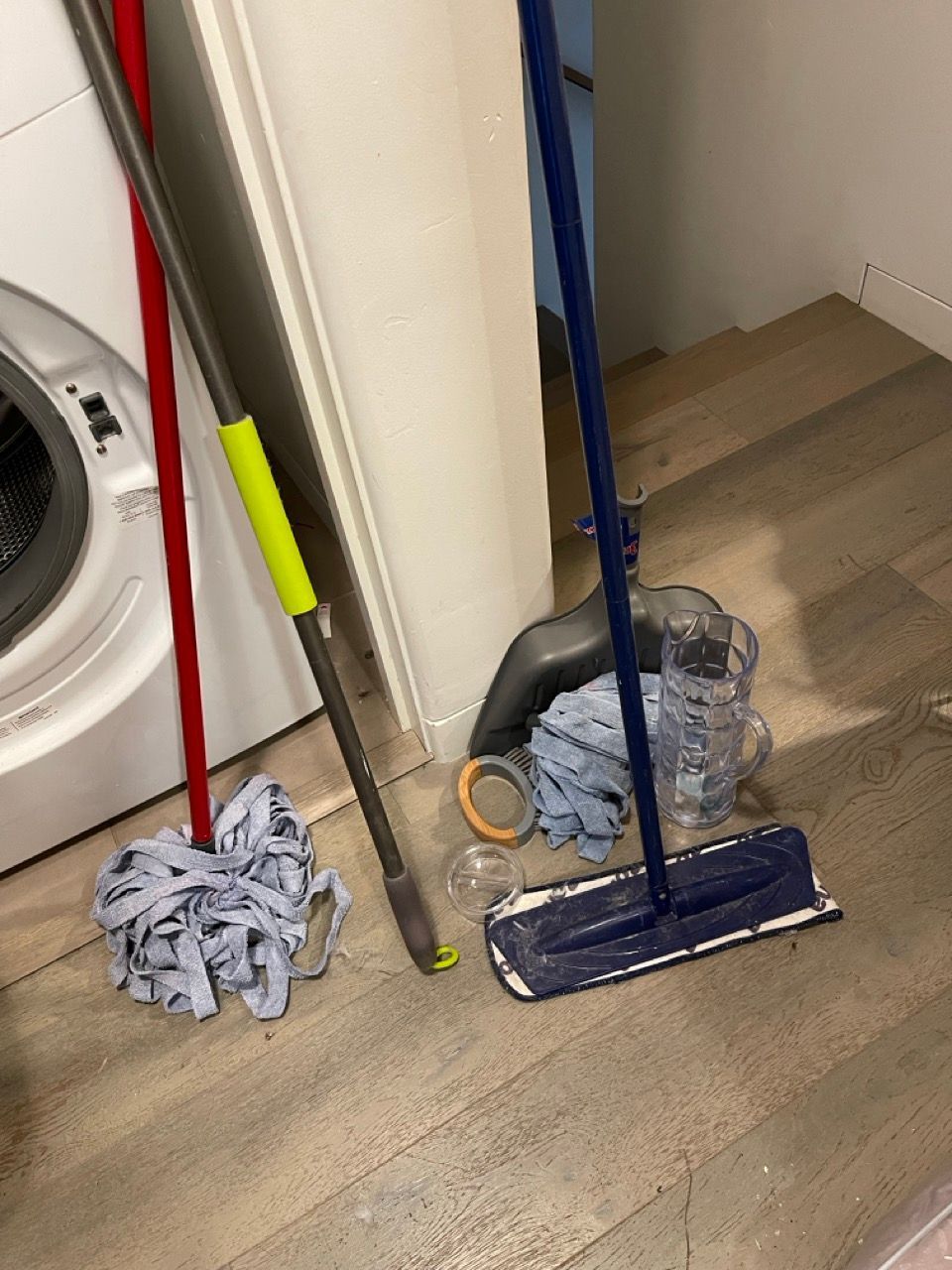 A mop and a broom are on the floor in a laundry room