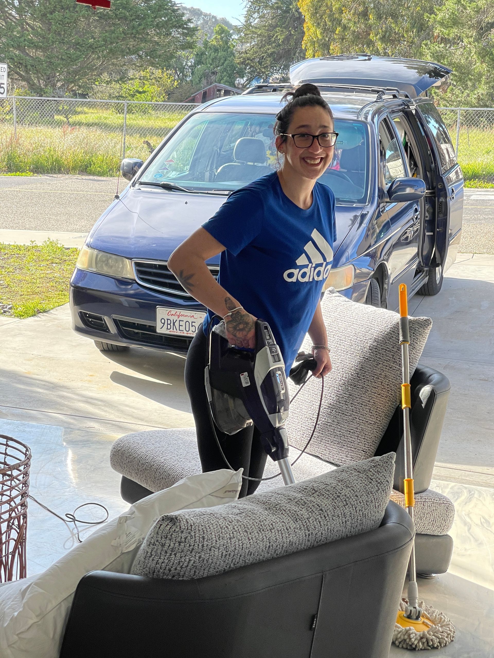 A woman is cleaning a couch with a vacuum cleaner.