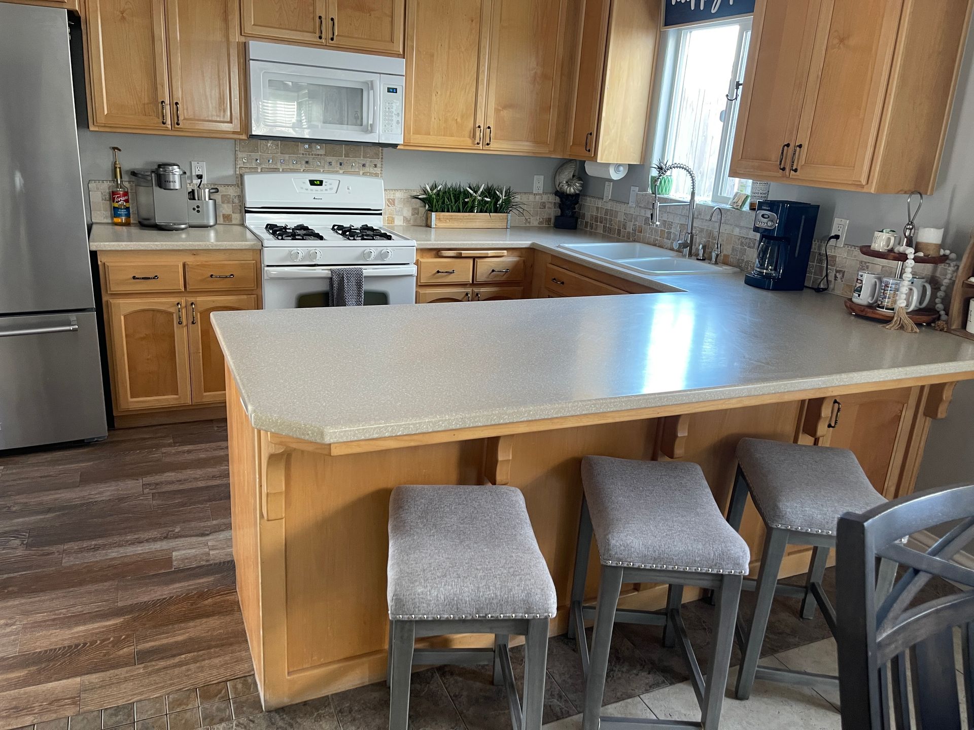 A kitchen with wooden cabinets , a stove , refrigerator , microwave , and stools.