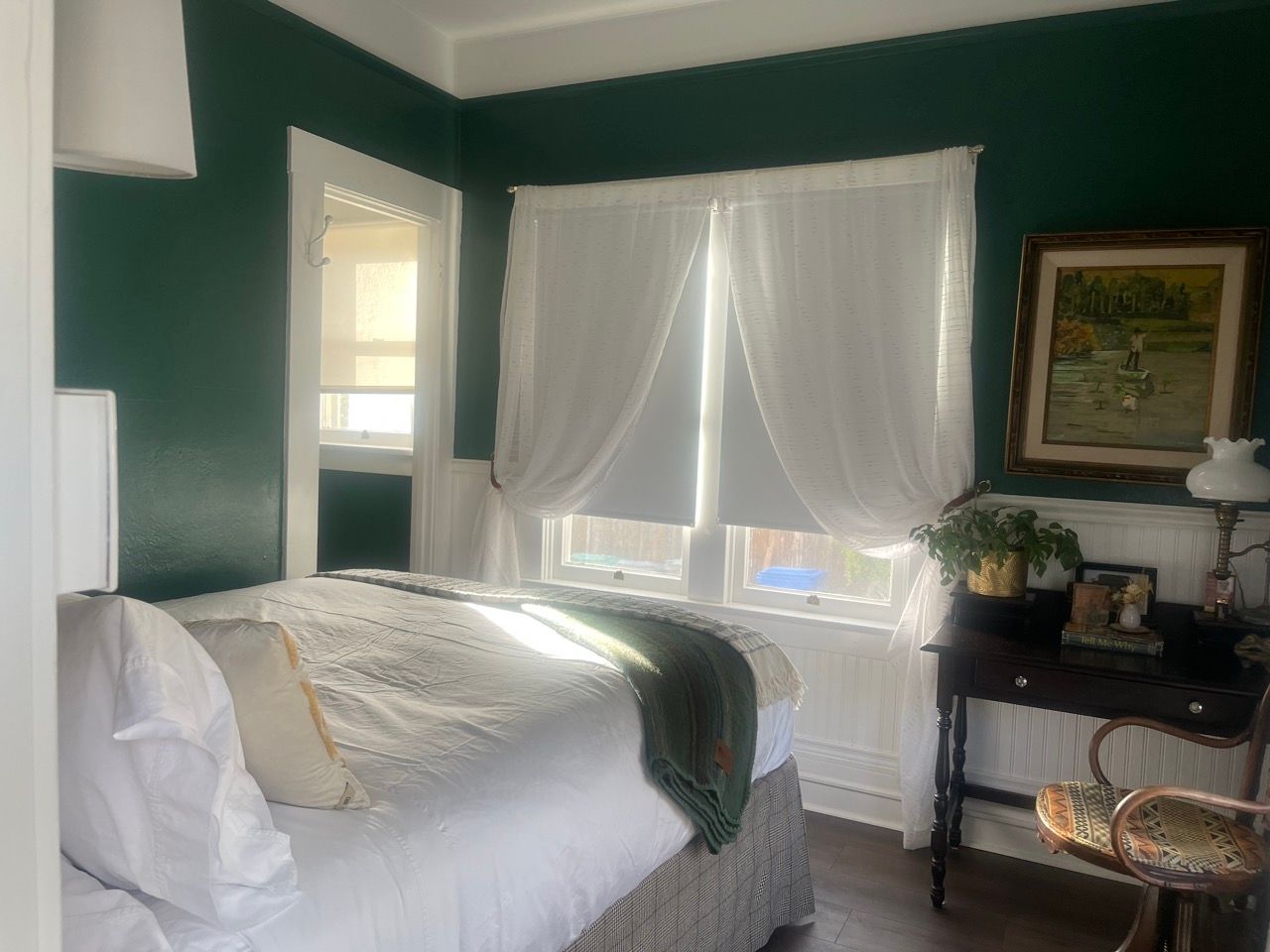 A bedroom with green walls and white curtains and a bed