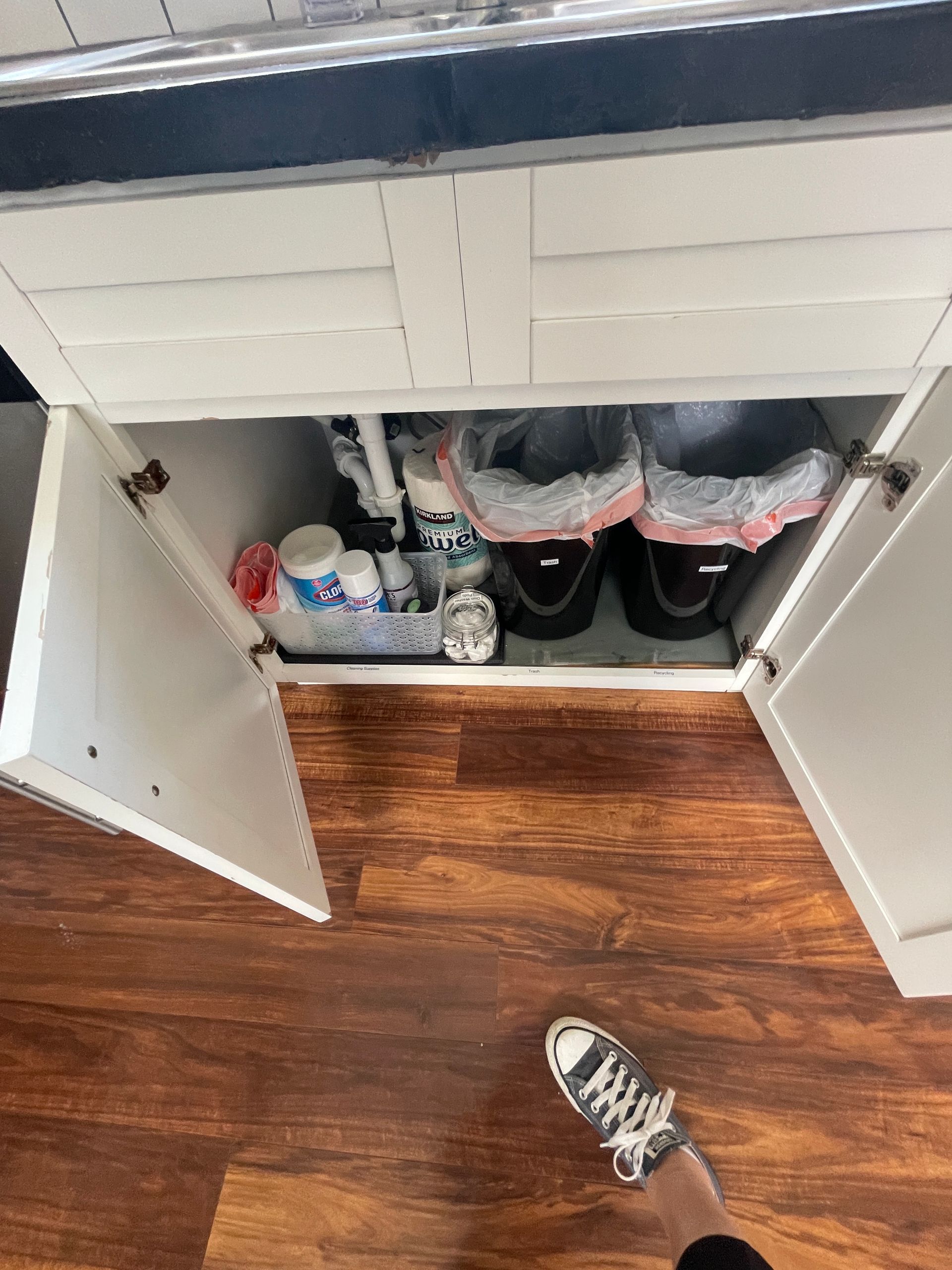 A person is standing in front of a cabinet with trash cans underneath it.