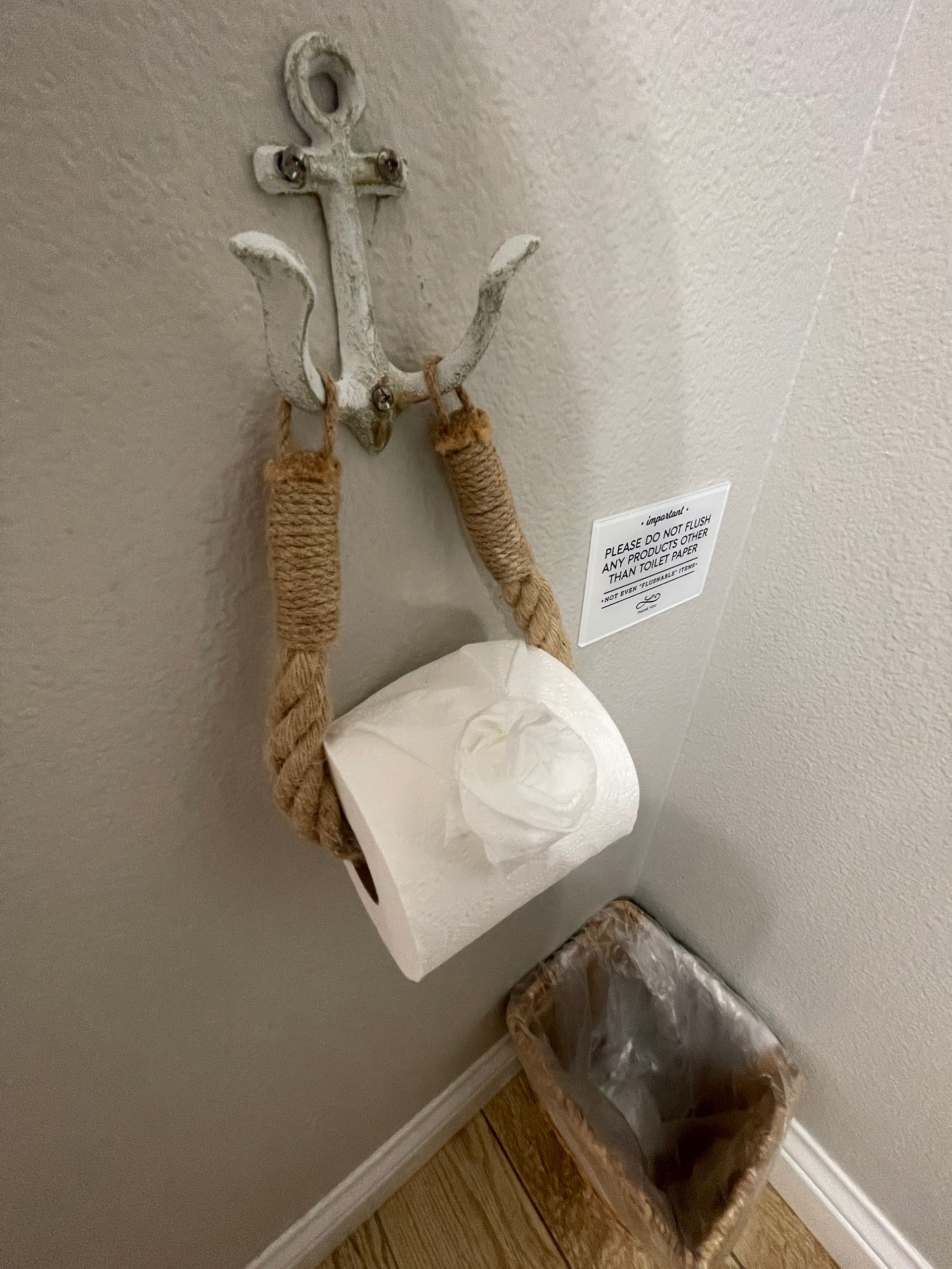 A toilet paper holder with a rope around it is hanging on a wall next to a trash can.