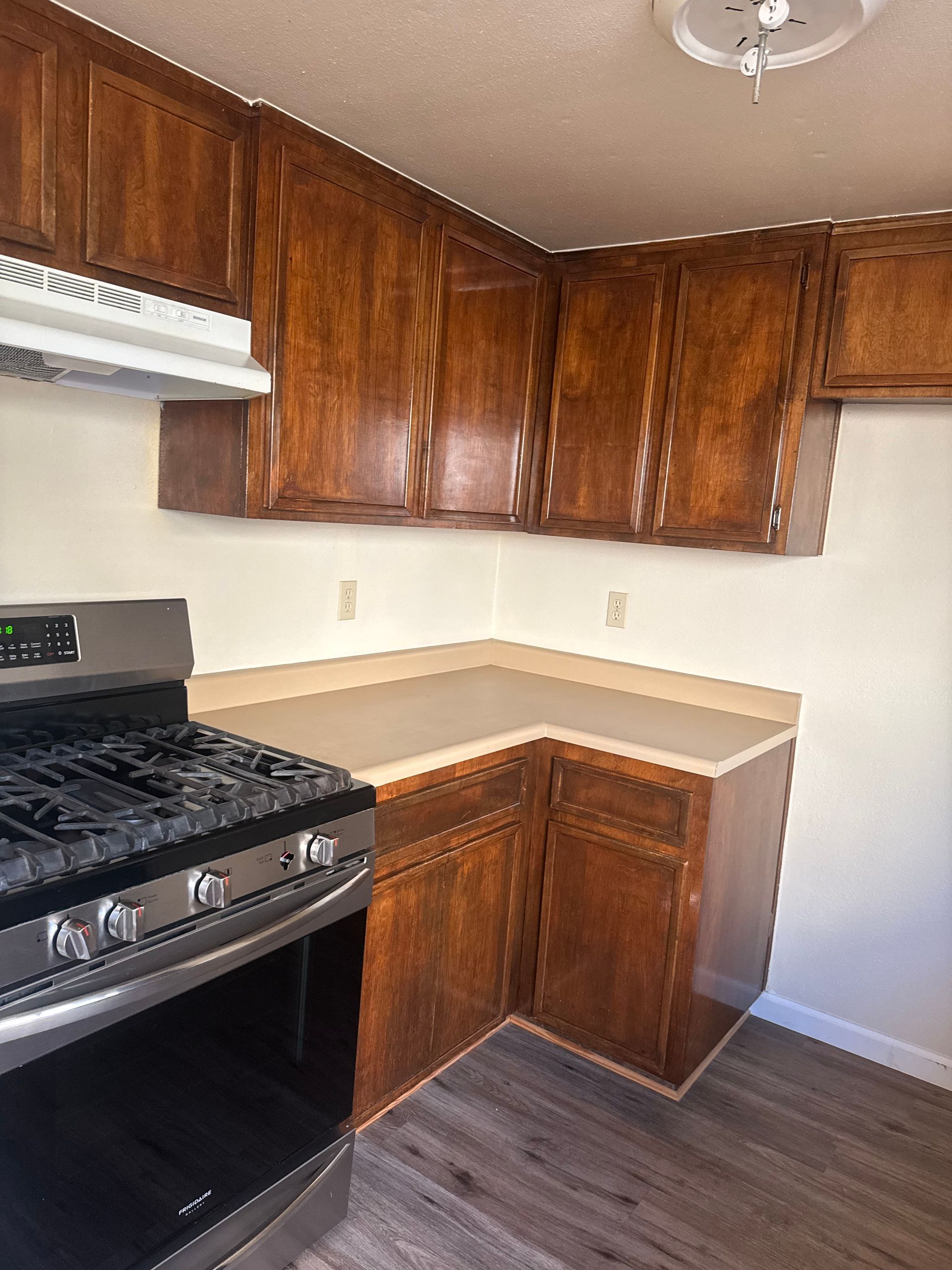 Kitchen with brown cabinets, beige countertops, a stainless steel stove, and gray wood-look flooring.