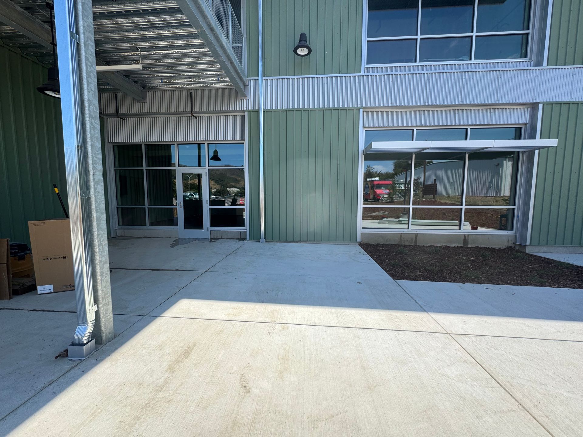 Exterior view of building with green siding, glass doors, and concrete patio.