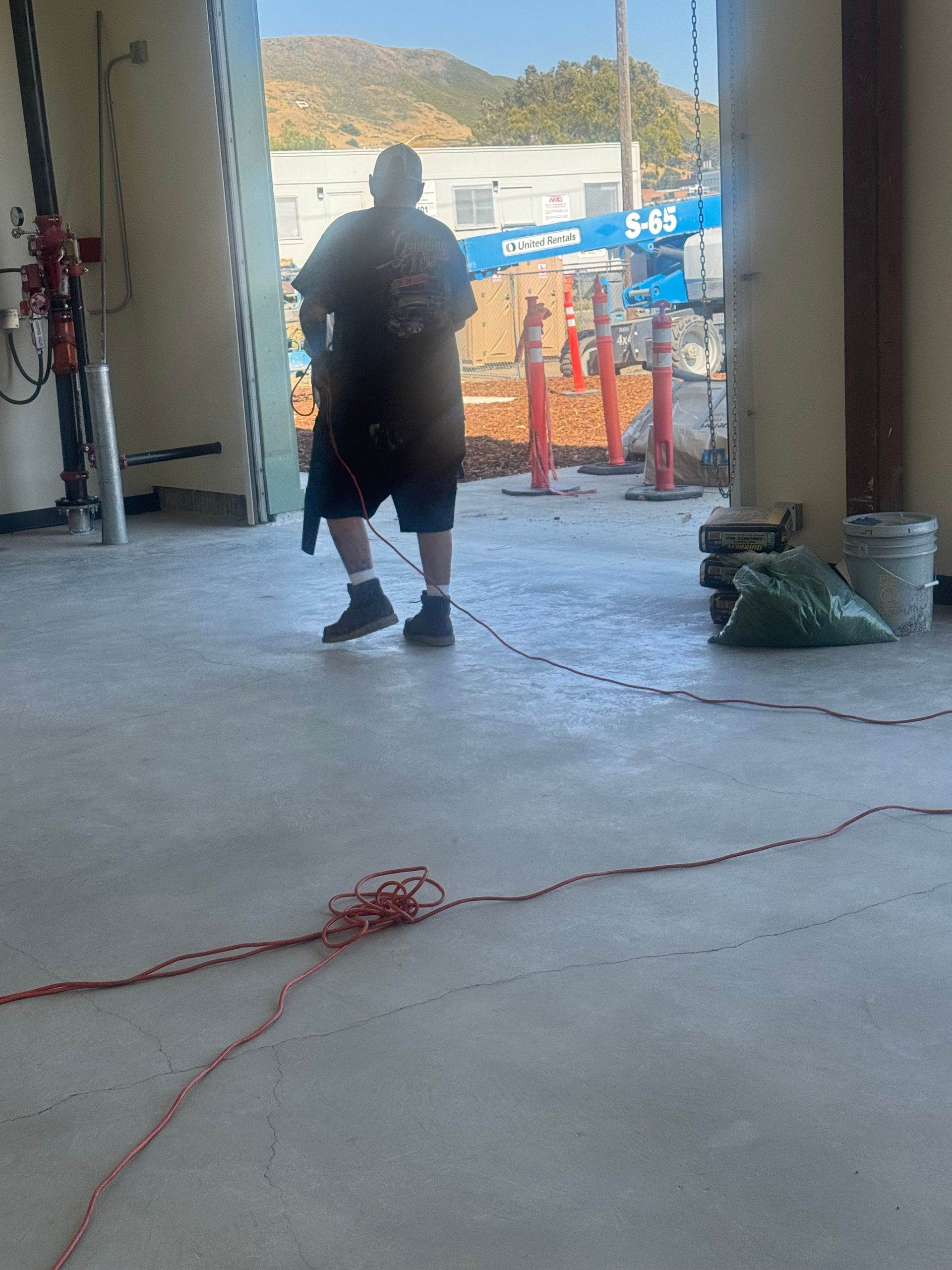 Man in a construction site, pulling a red cord across a concrete floor.