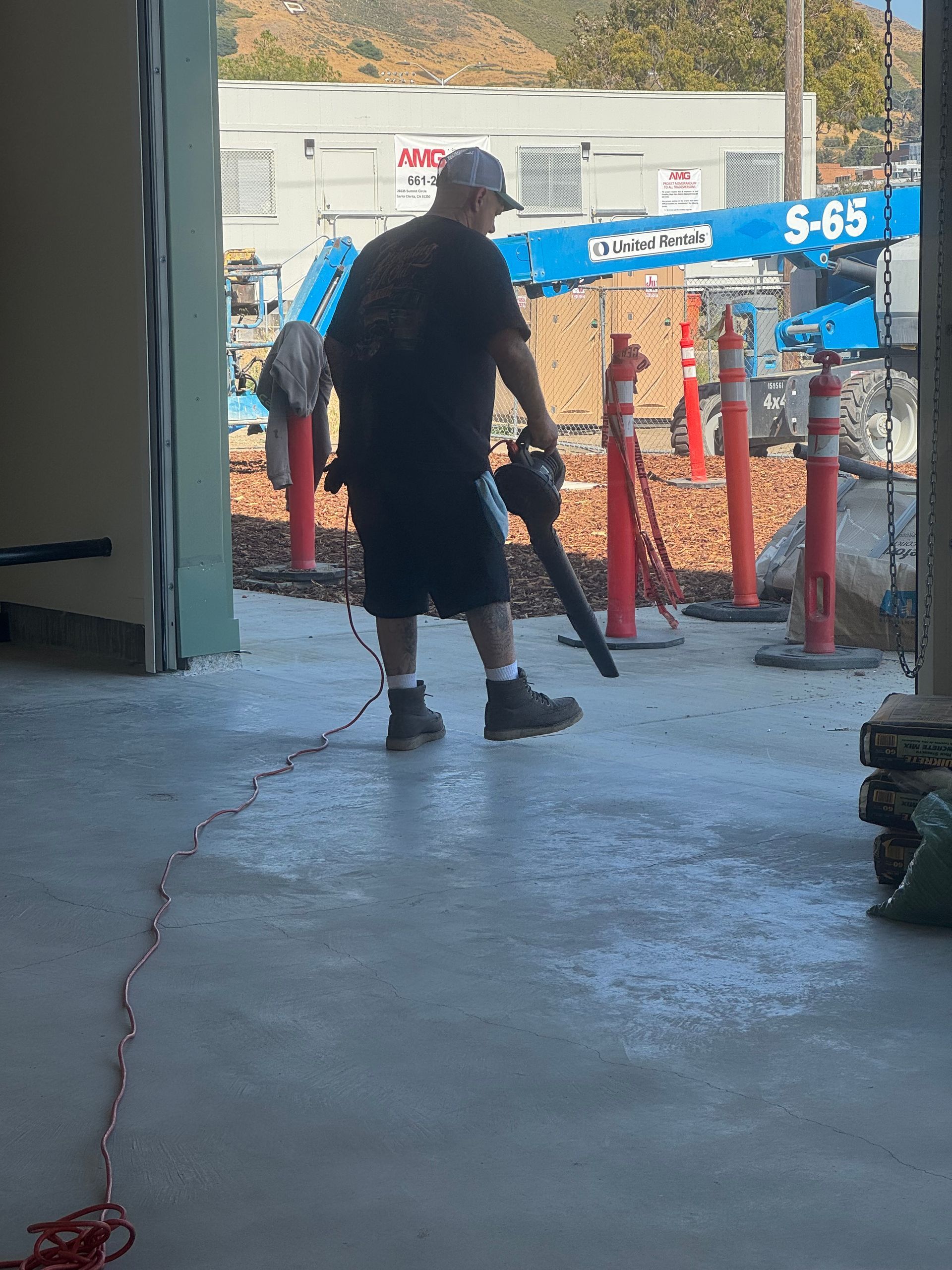 Man using a leaf blower on a concrete surface, likely cleaning a construction site.