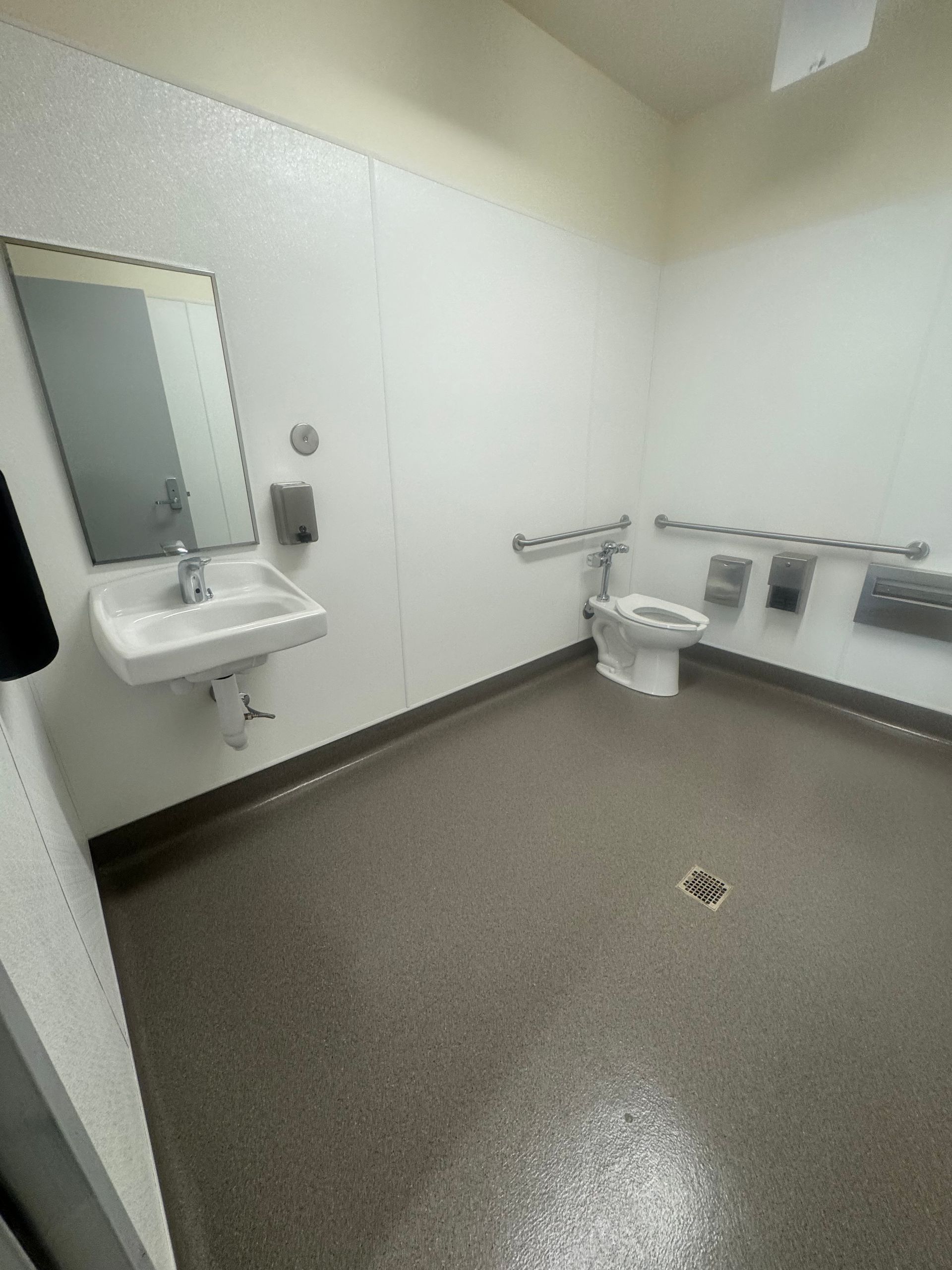 Accessible bathroom with sink, toilet, and grab bars. Gray floor, white walls, and mirror.