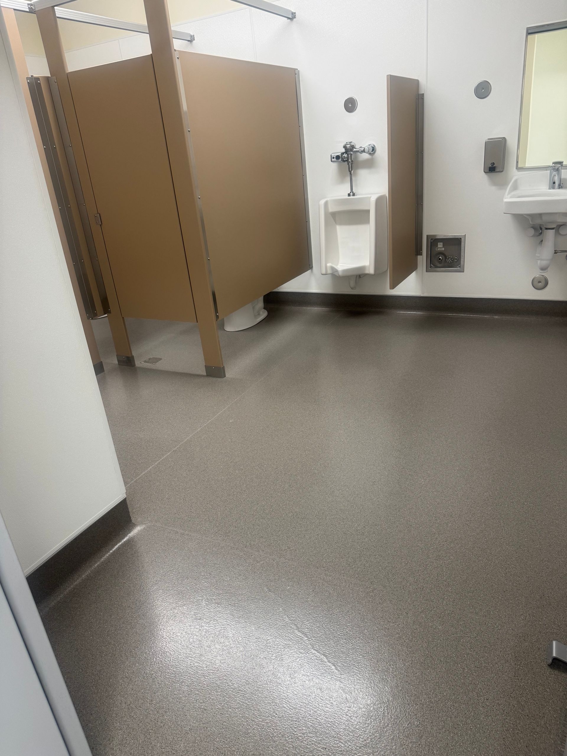Public restroom with stalls, a urinal, and a sink, all on a speckled gray floor.