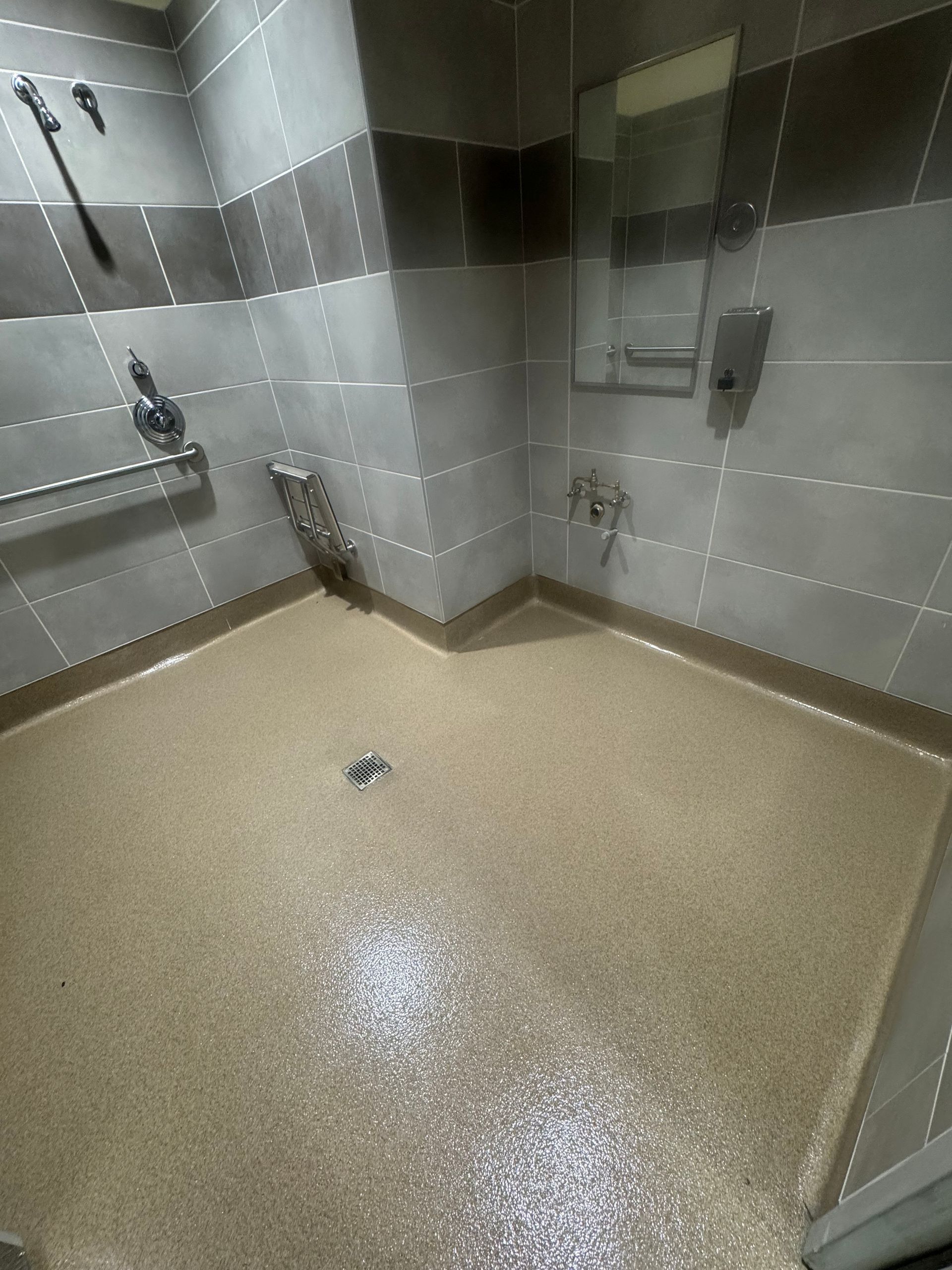 Accessible shower with beige floor, gray tile walls, and silver fixtures.