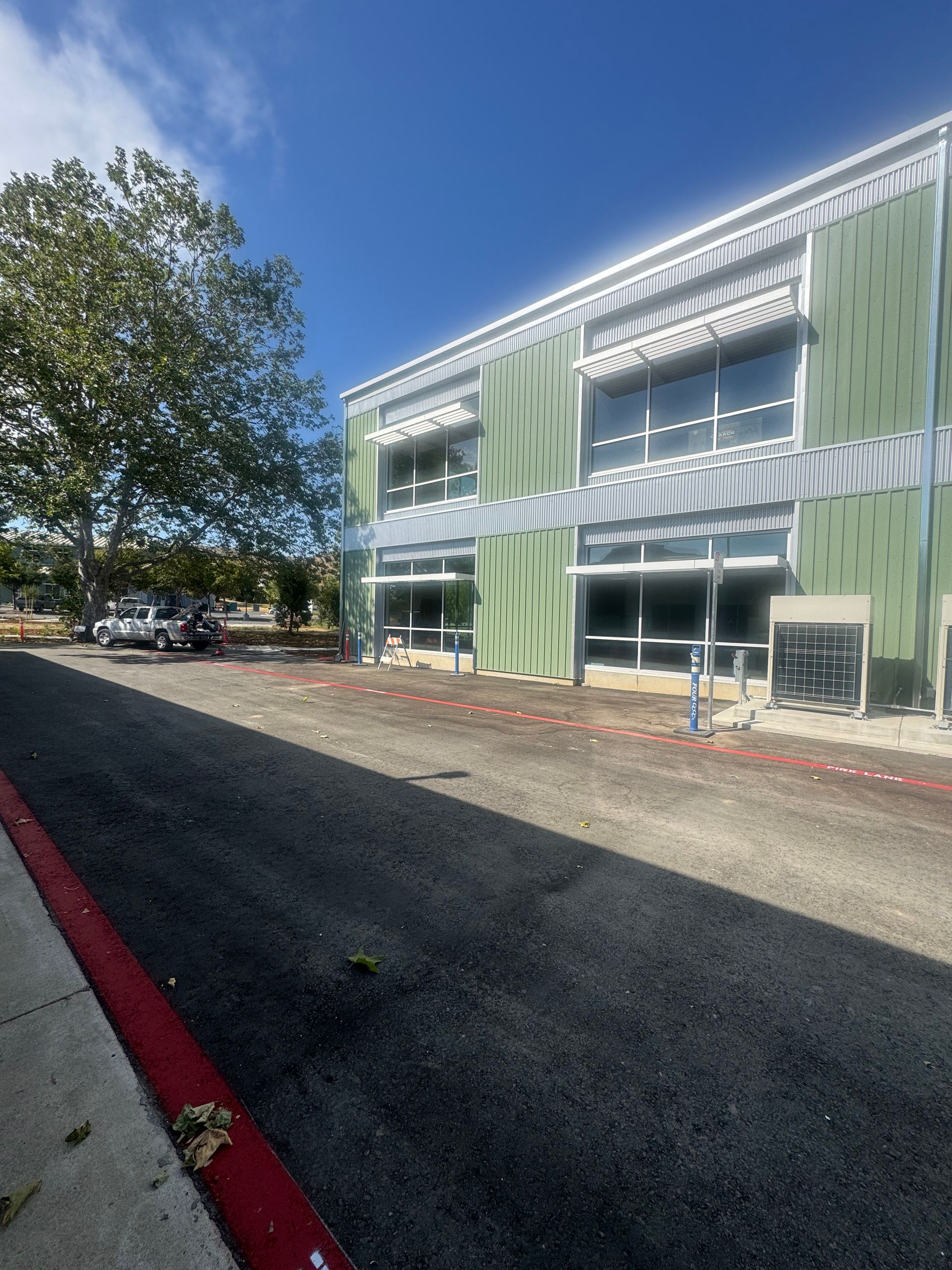 Building under construction with green panels, large windows, and a newly paved asphalt area. Blue sky.