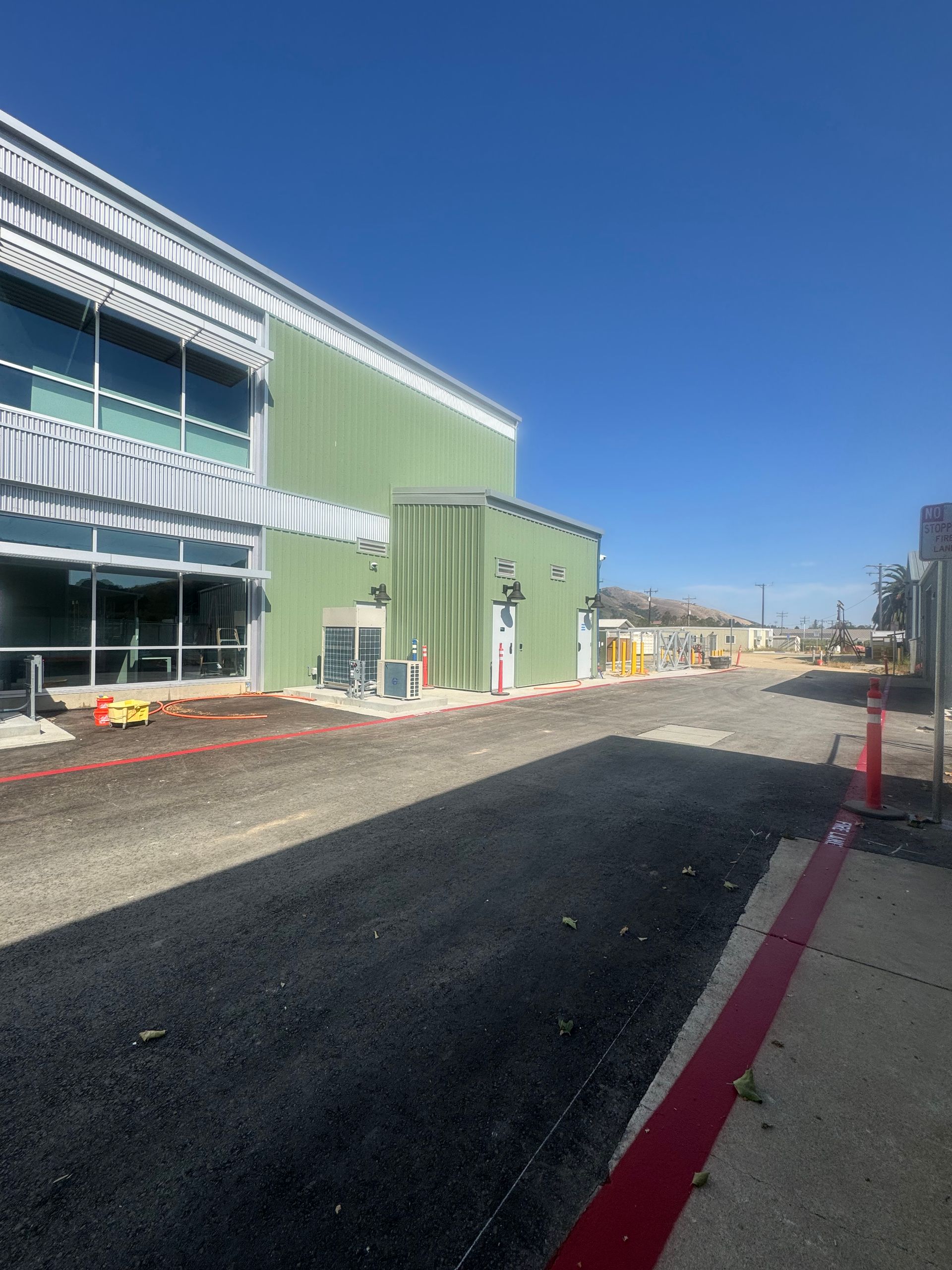 Green building with asphalt path, red curb, and blue sky. Construction in progress.