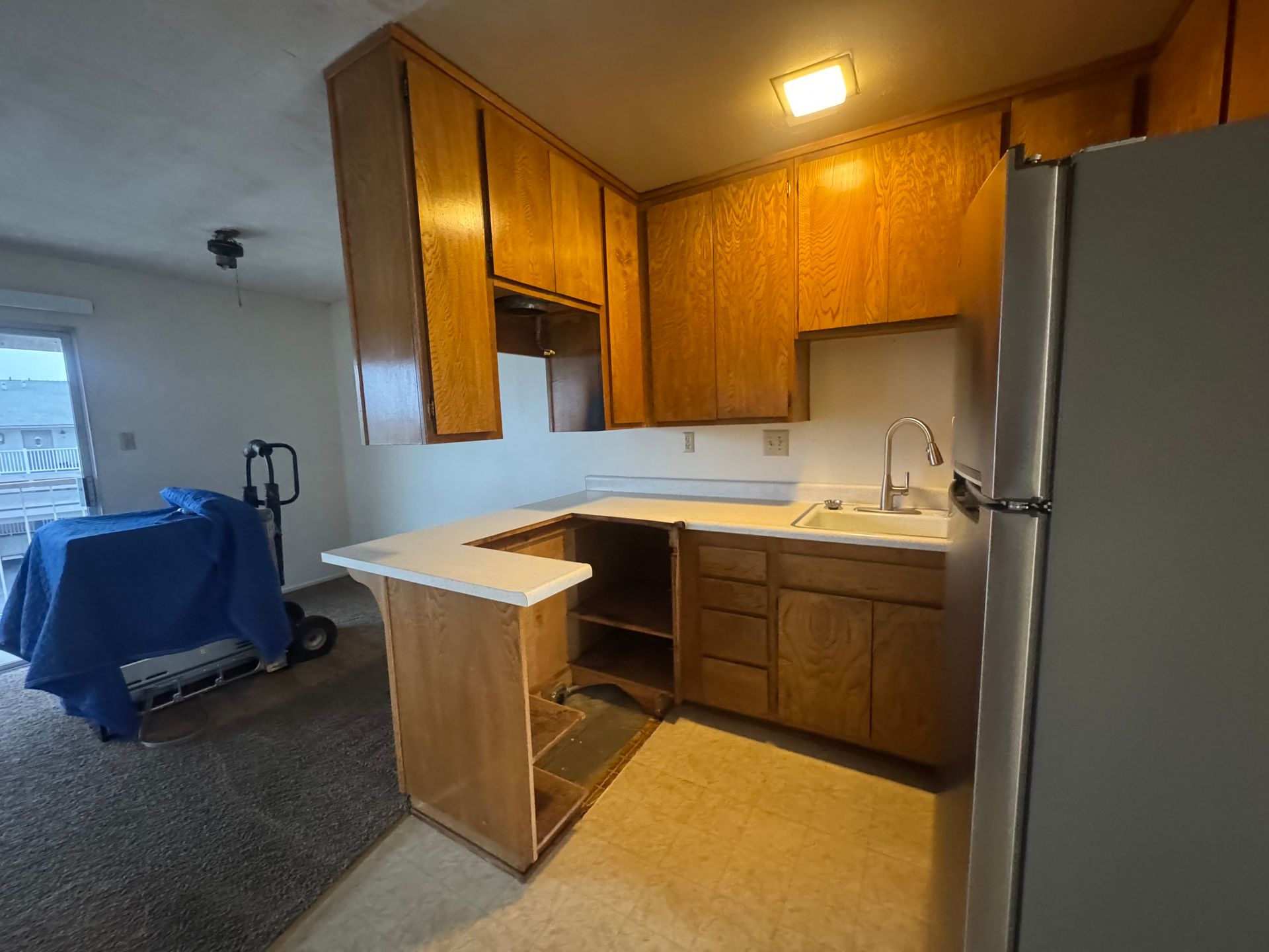 A small kitchen with wood cabinets, a countertop, sink, and a refrigerator.