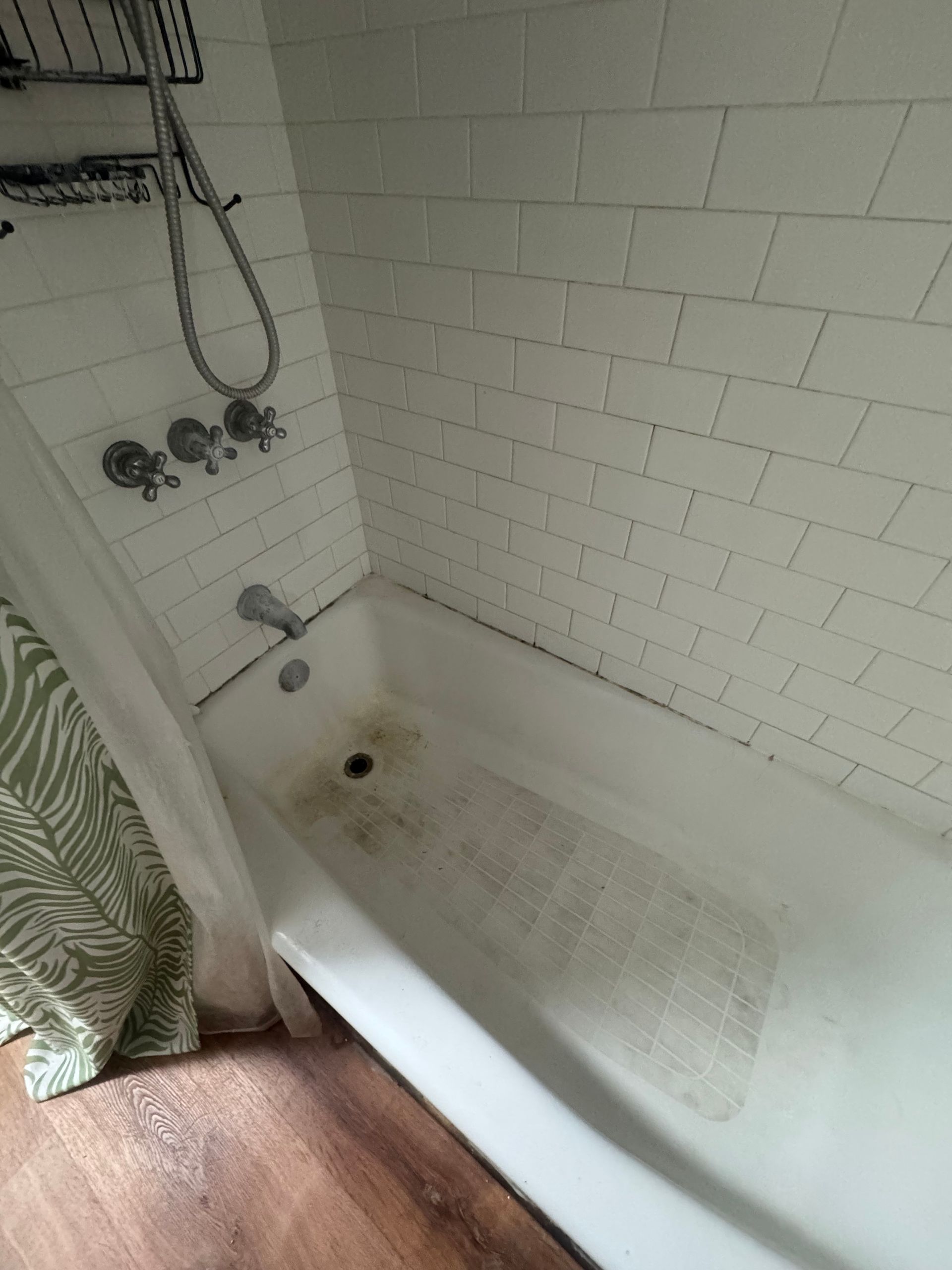 White tiled shower/tub with discoloration, showerhead, and a partially visible curtain.