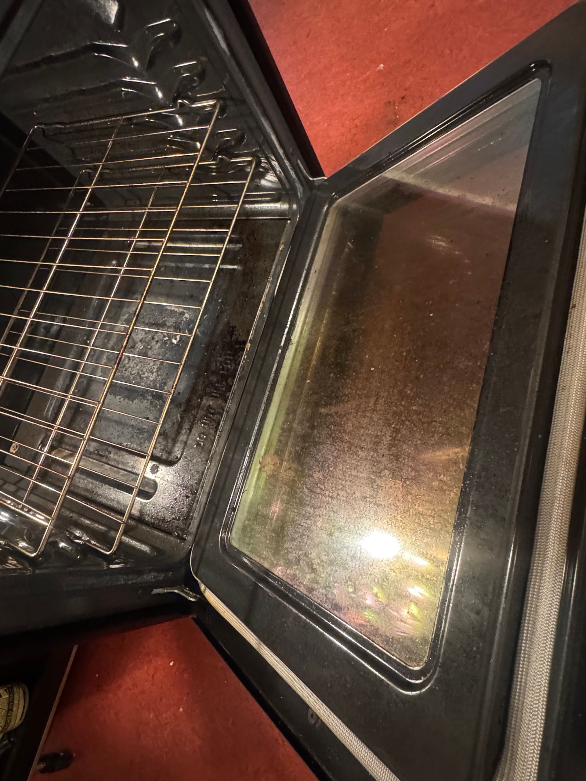 Open oven with dirty, greasy glass door and racks. Interior has residue and debris.