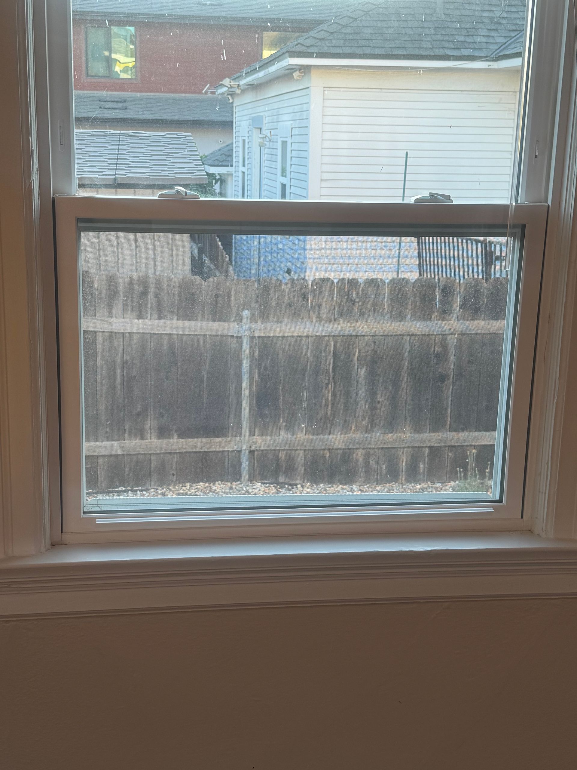 A window looking out at a wooden fence and a partially visible building.