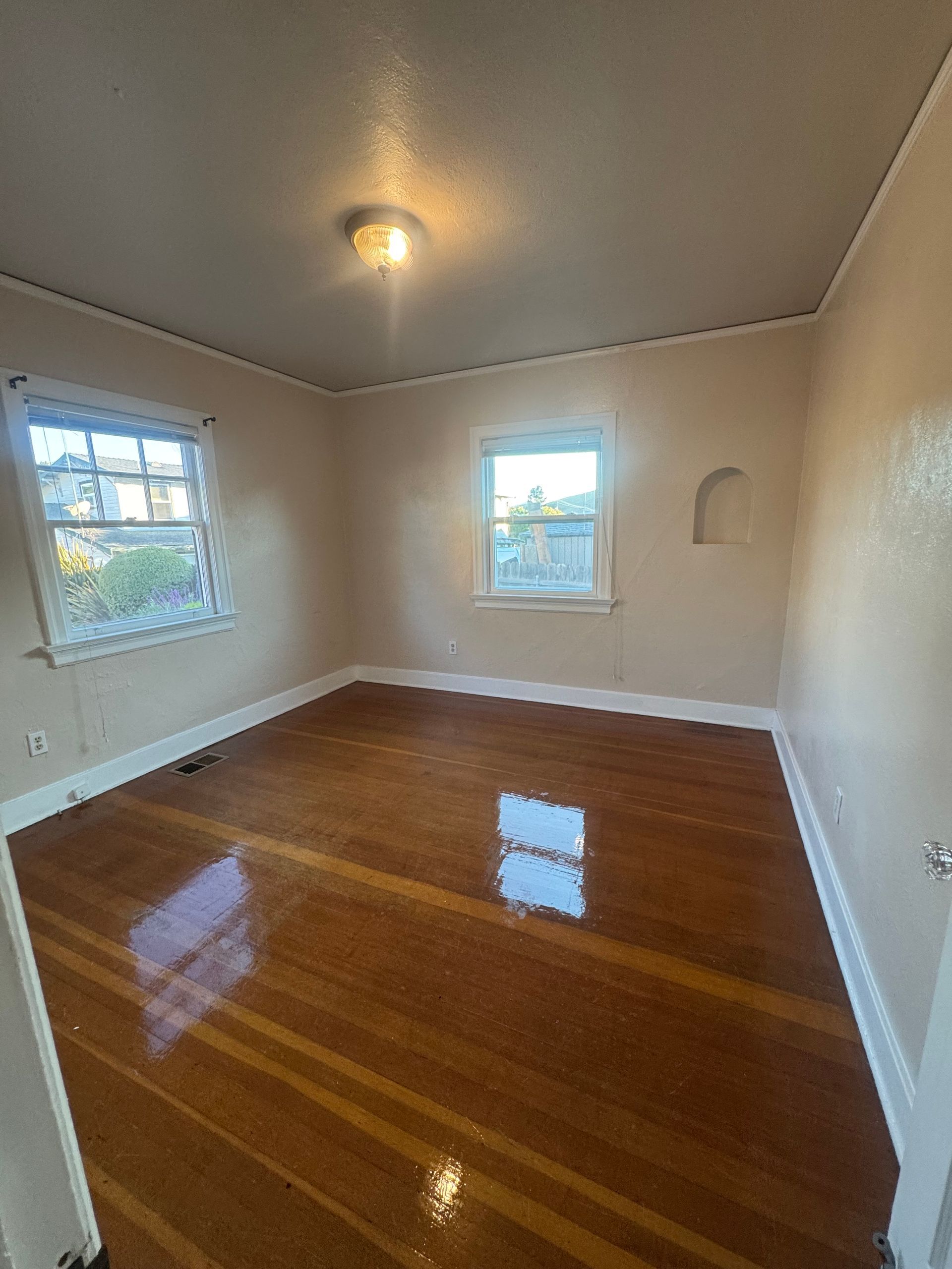 Empty room with glossy wood floor, two windows, and a recessed shelf.