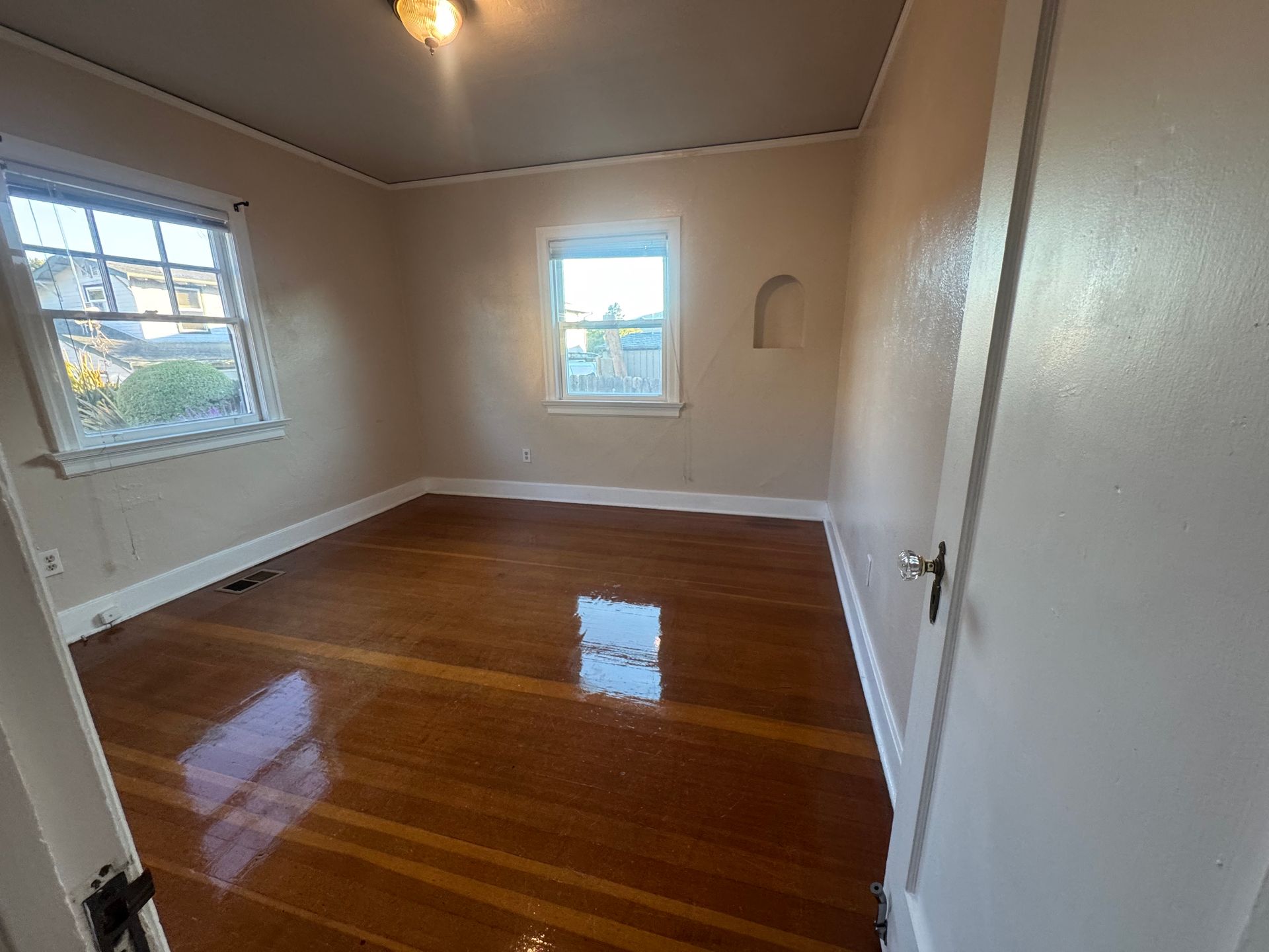 Empty bedroom with hardwood floors, two windows, and a light fixture.