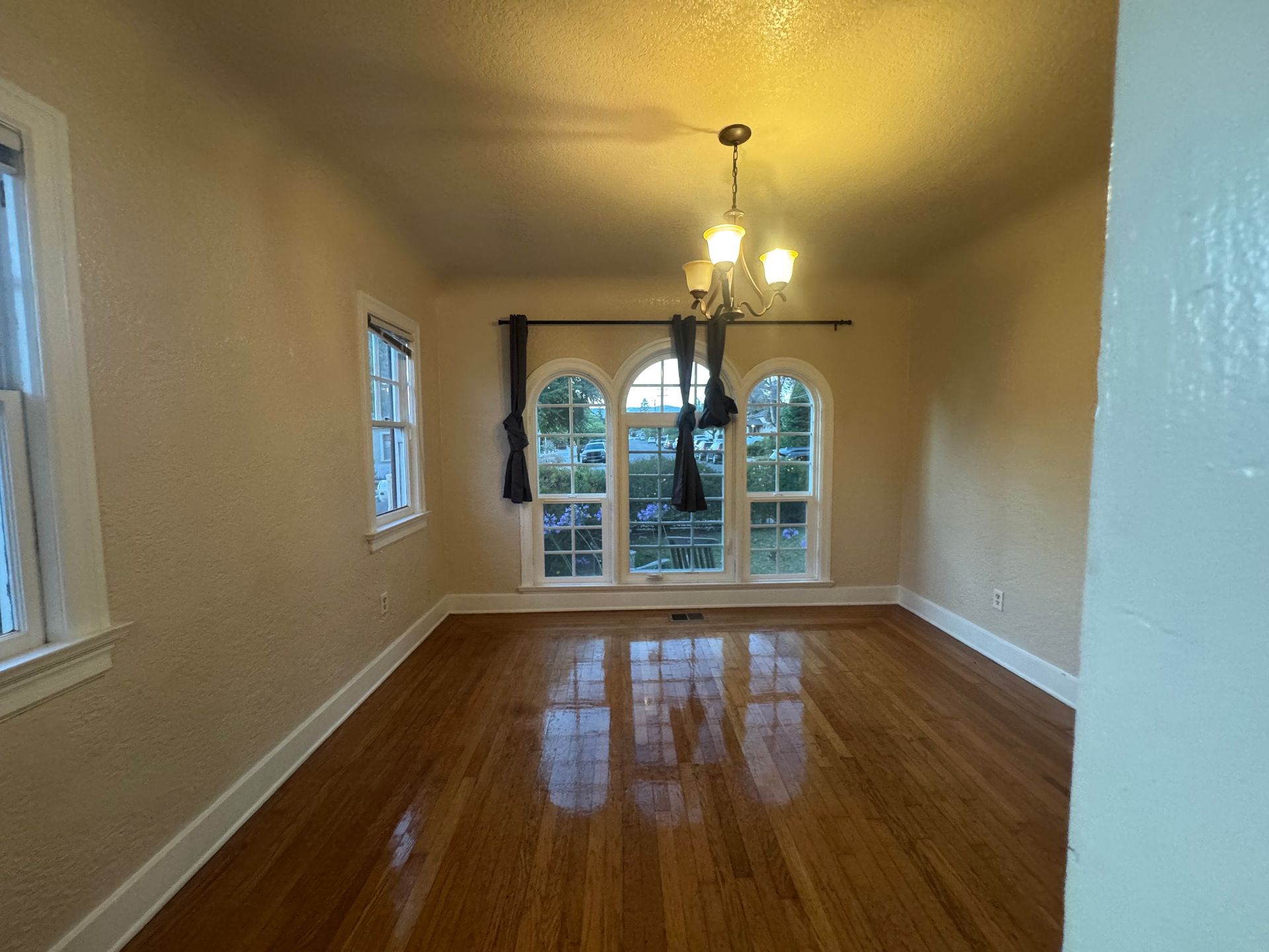 Empty dining room with hardwood floors, arched windows, and chandelier.