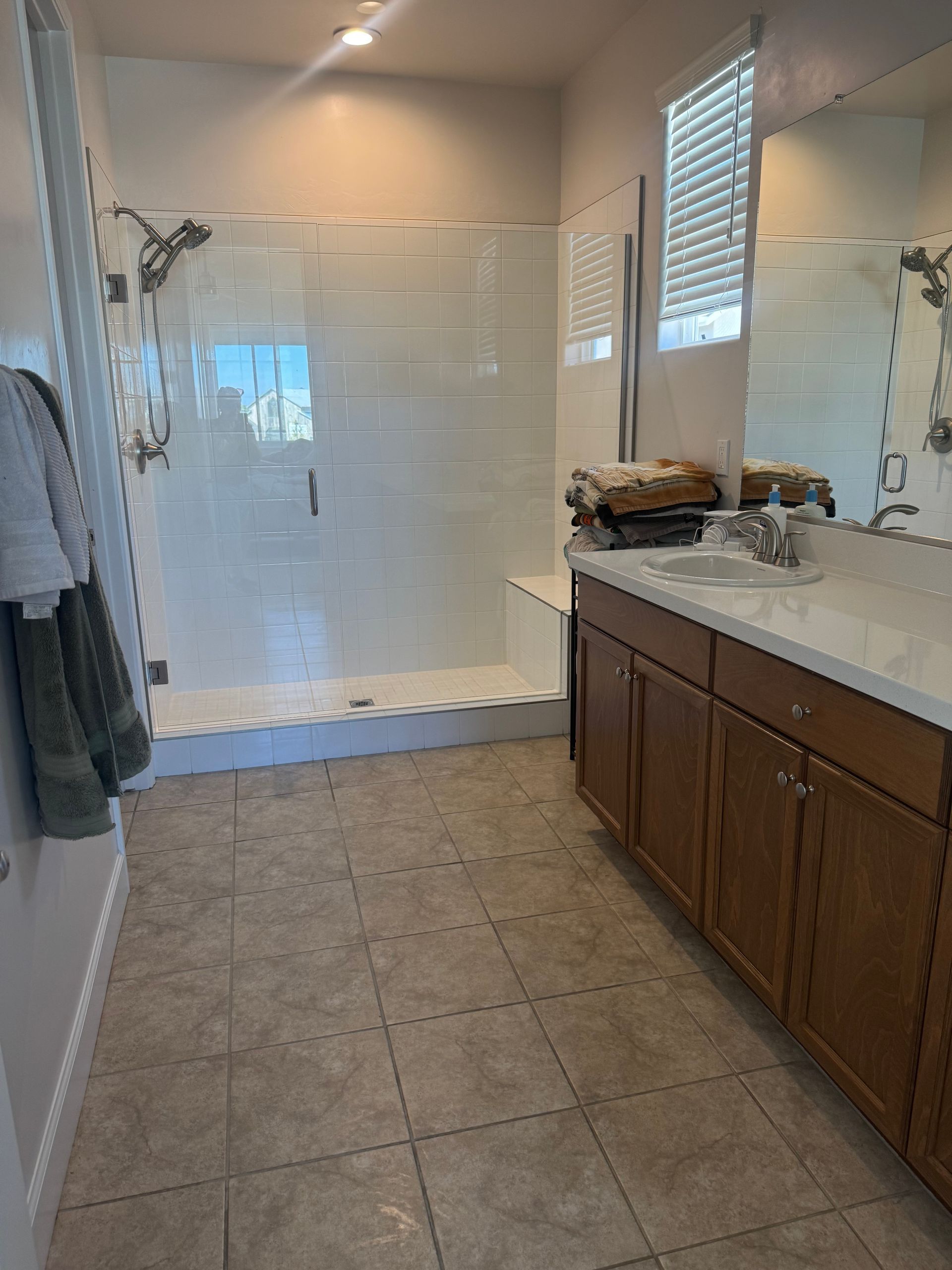 Bathroom with glass shower, vanity, brown cabinets, tiled floor, and towels hanging.