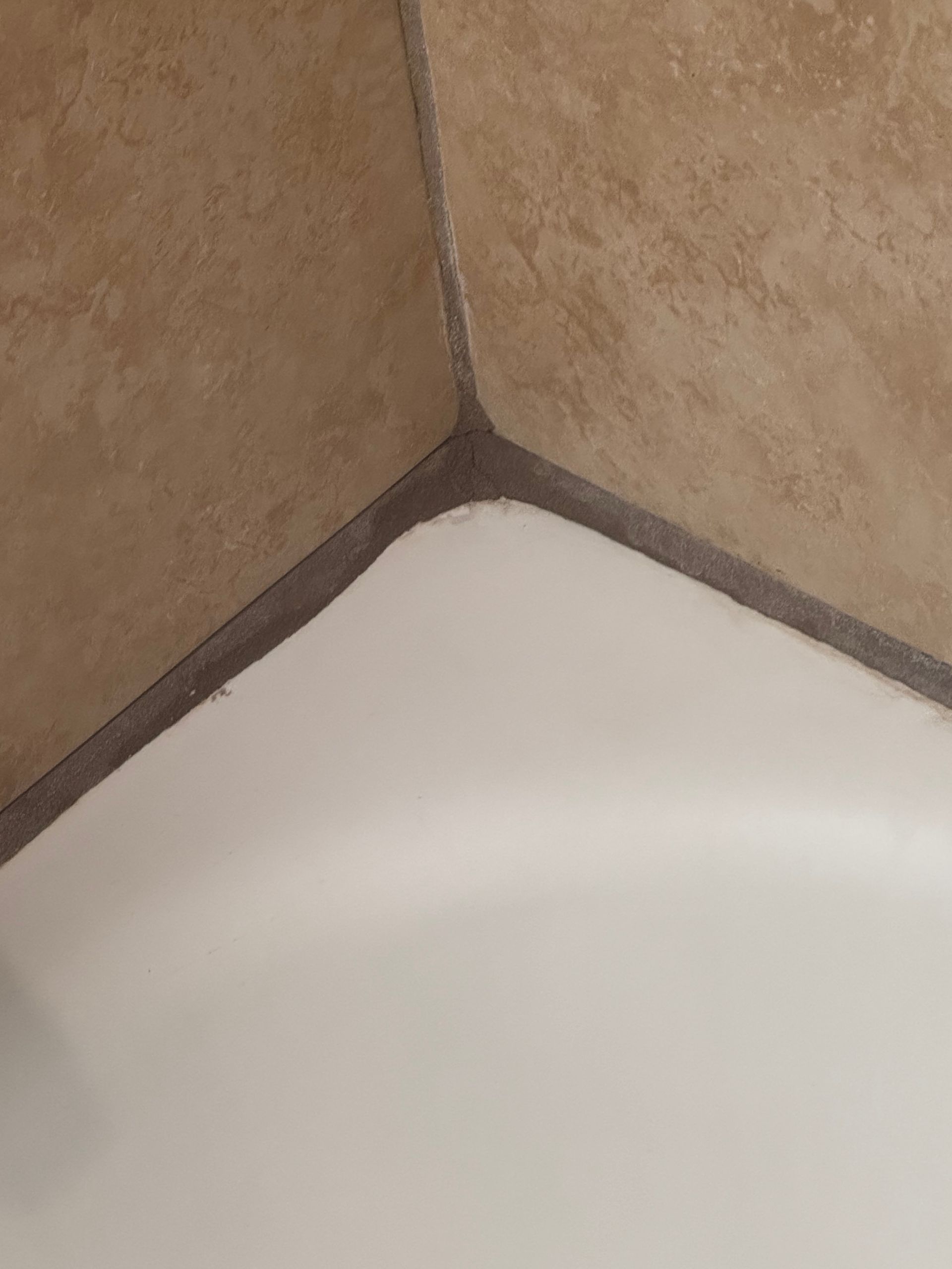 Brown tiled corner meeting a white surface, sealed with dark caulk.
