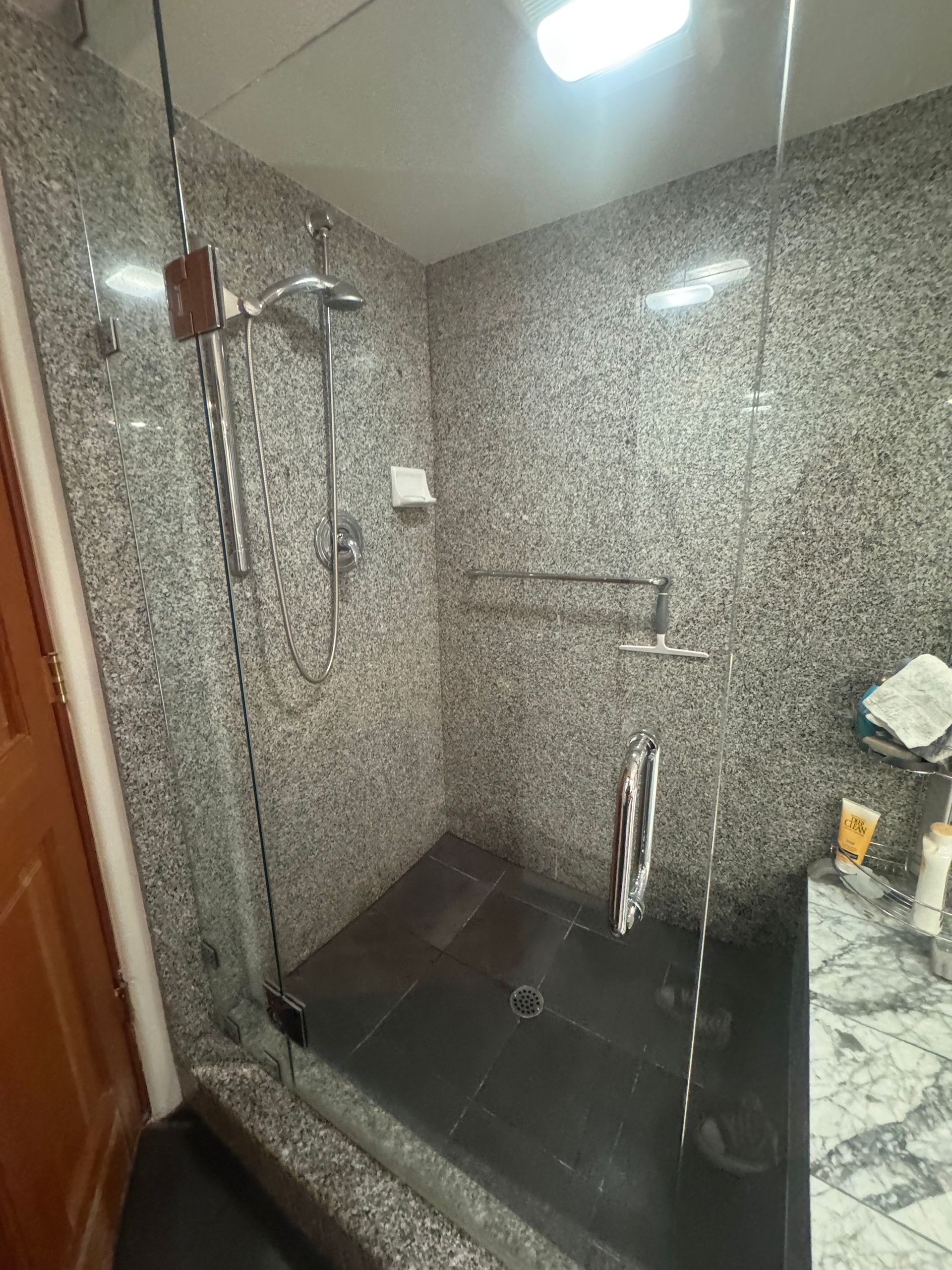 A walk-in shower with gray speckled tile walls and a dark tiled floor; glass door and chrome fixtures.