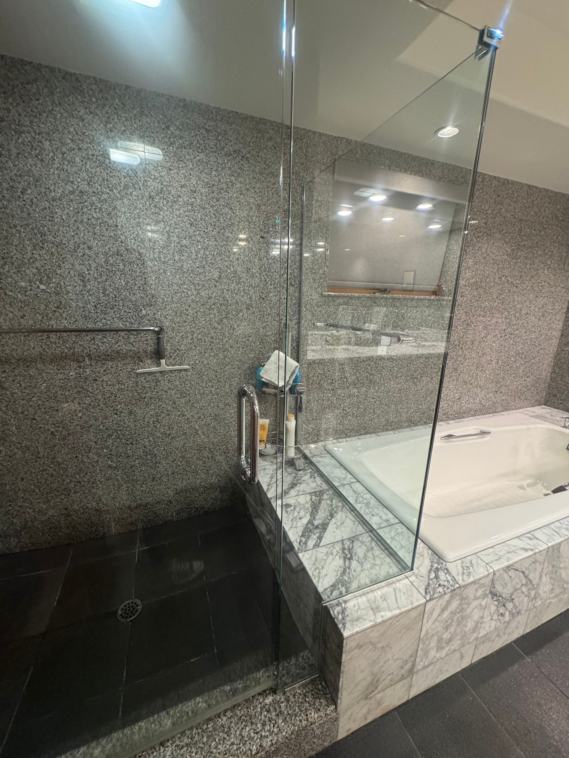 Bathroom with a gray tiled shower and tub area; glass enclosure; black floor tiles.