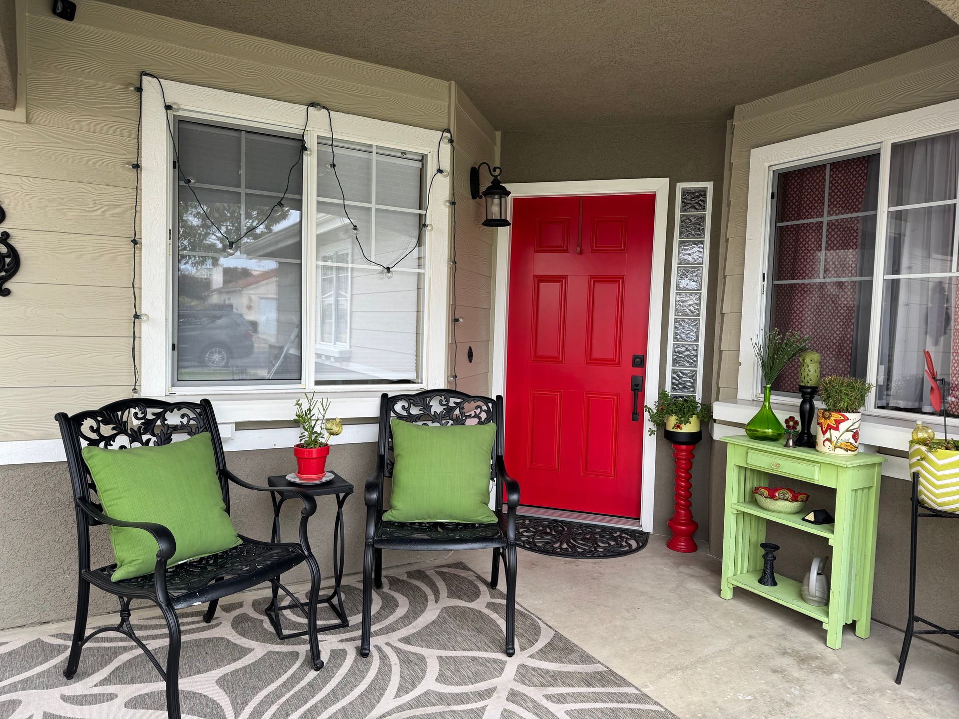 A front porch with red door, black chairs, green cushions, and a lime green shelf.