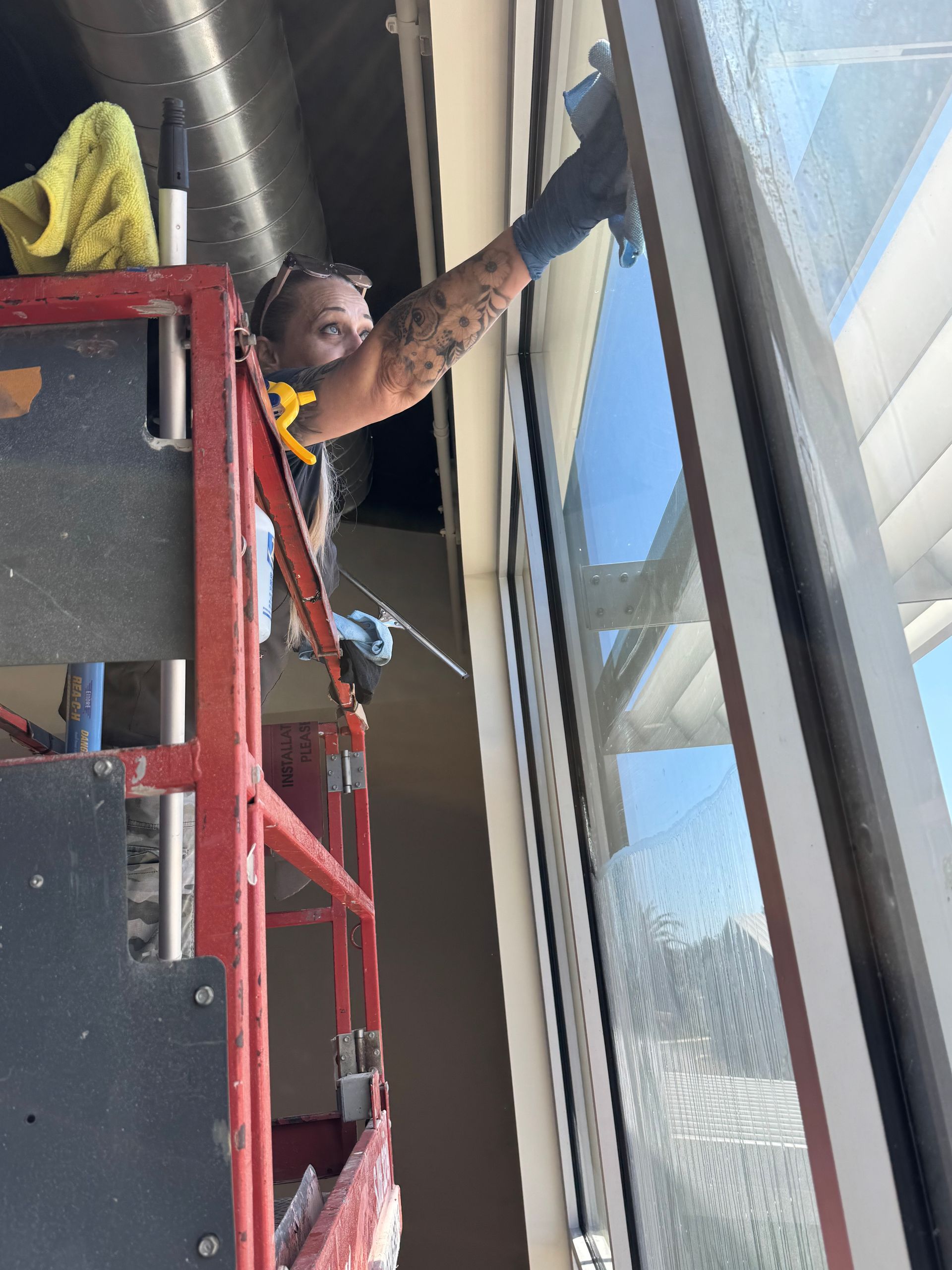 Person on a lift washing a large window; blue sky visible through the glass.