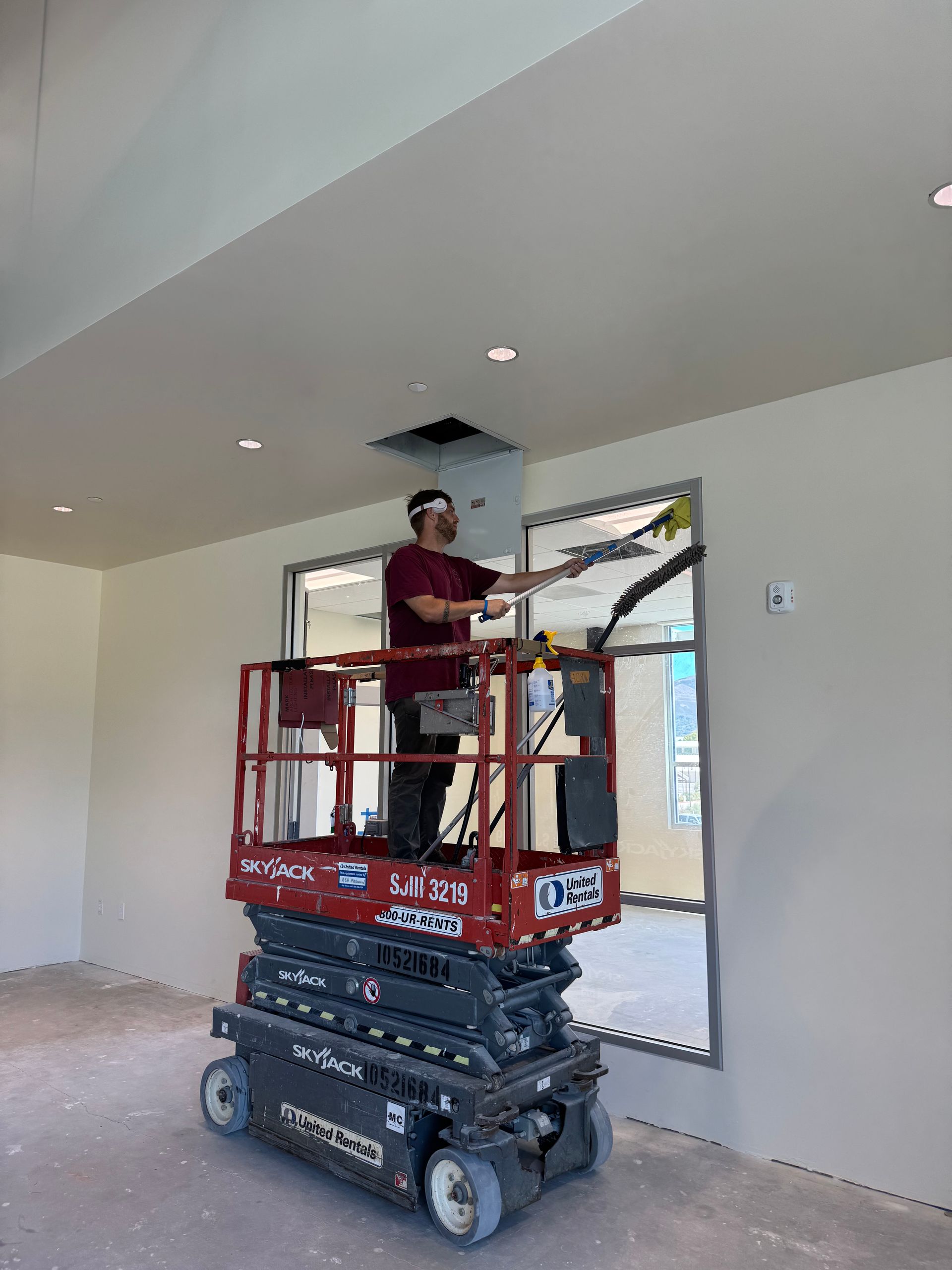 Man on a scissor lift reaching into a ceiling opening with a tool in an unfinished room.