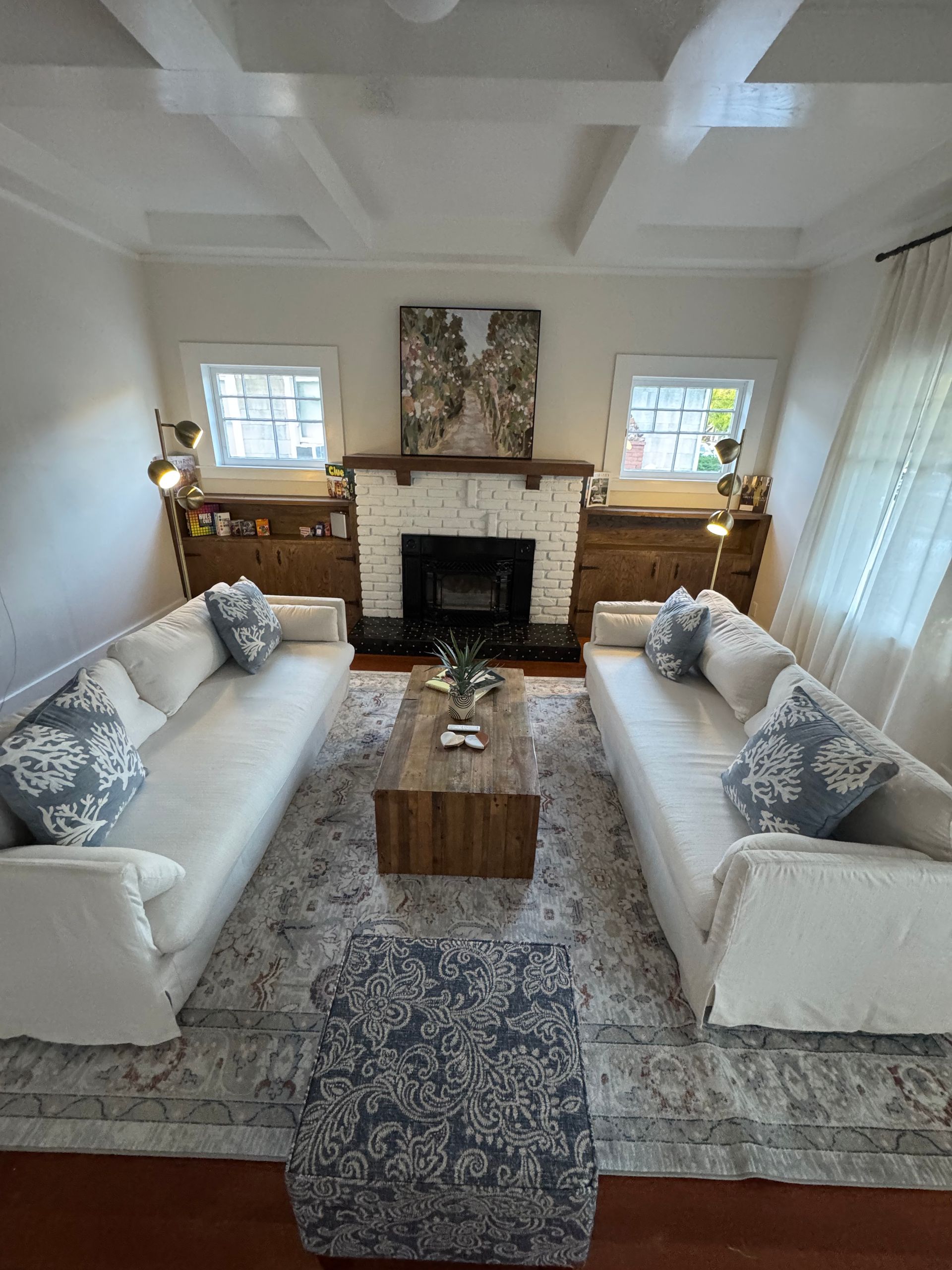 Living room: Two white sofas face fireplace, neutral rug, wooden coffee table, blue patterned pillows and ottoman.
