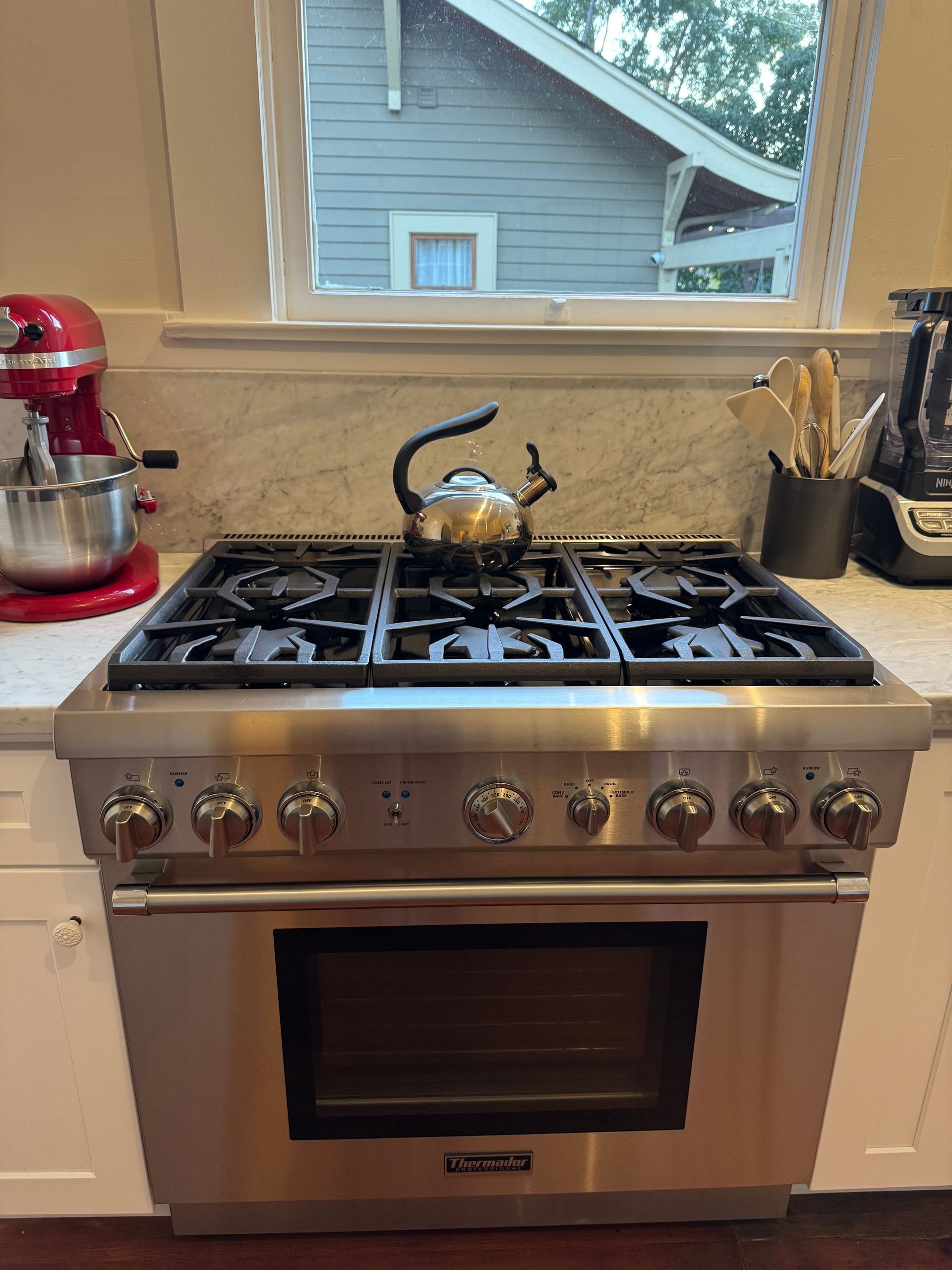 Stainless steel range with a kettle on top in a kitchen. Window in the background.