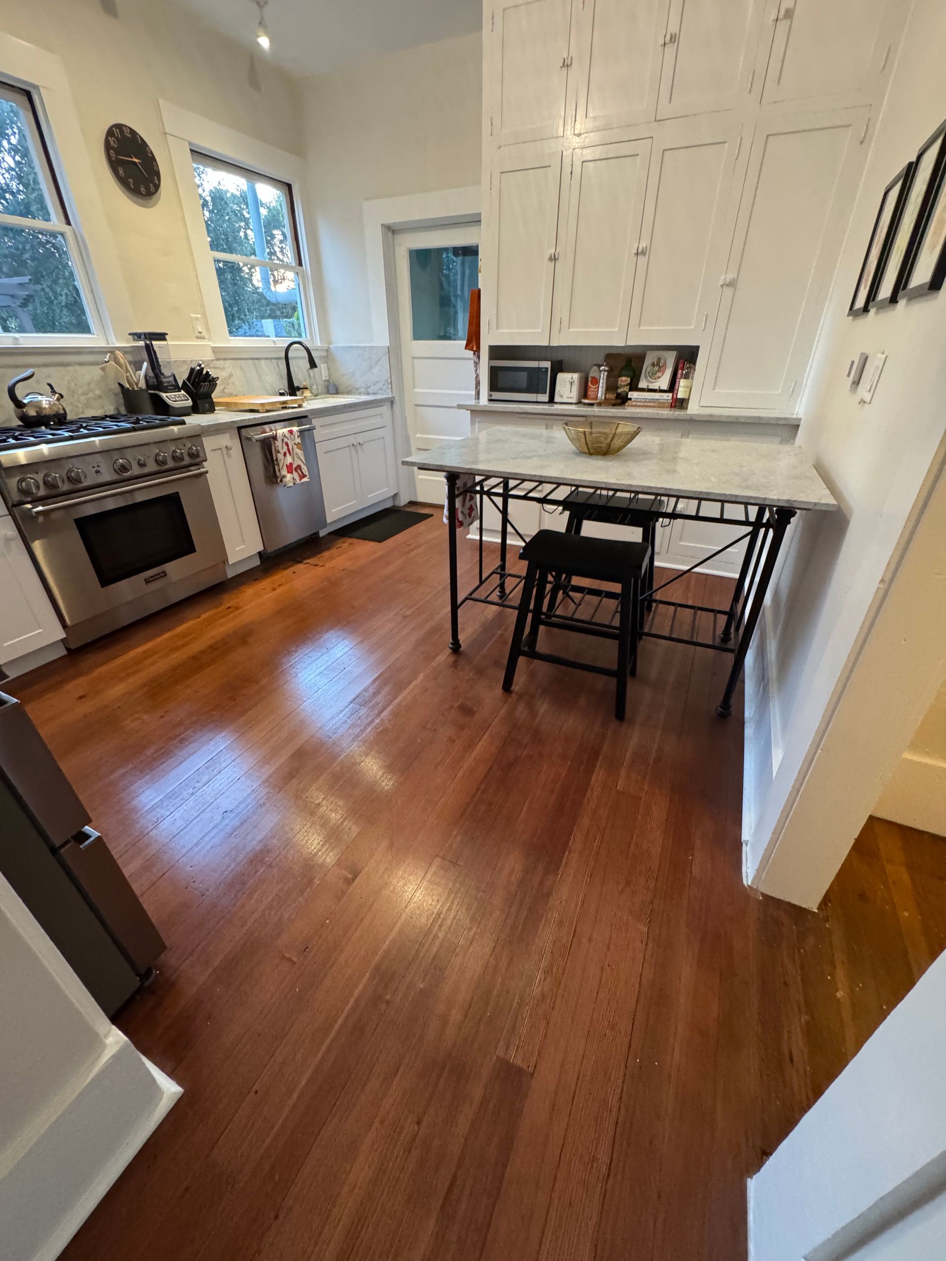 Kitchen with hardwood floors, stainless steel appliances, and white cabinets. A table with stools is present.