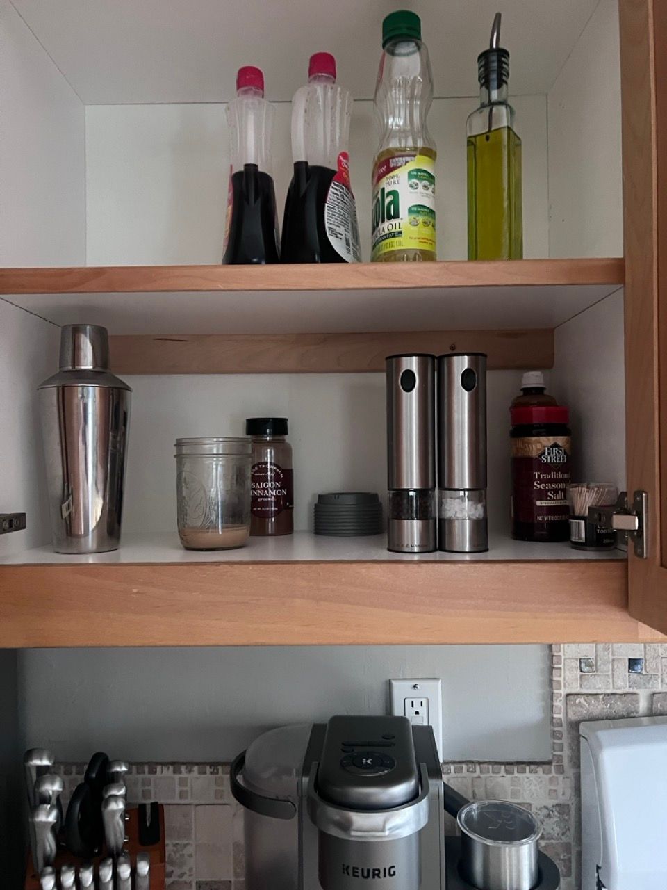 A kitchen cabinet filled with bottles and a keurig coffee maker
