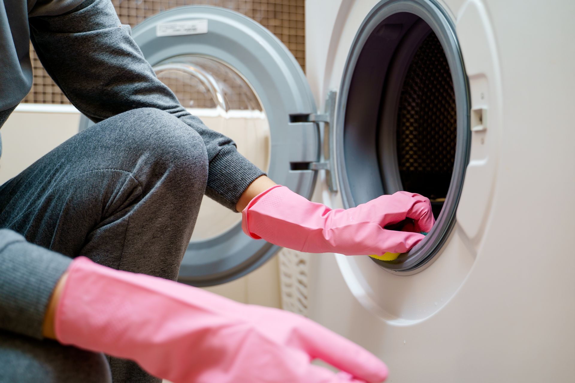 A person wearing pink gloves is cleaning a washing machine.