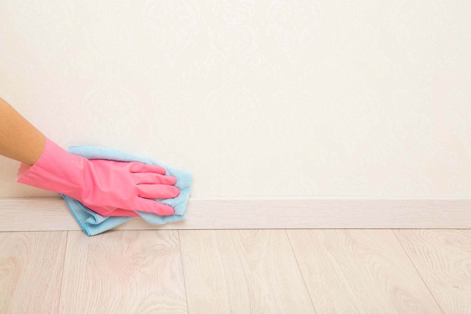 A person wearing pink gloves is cleaning the floor with a cloth.