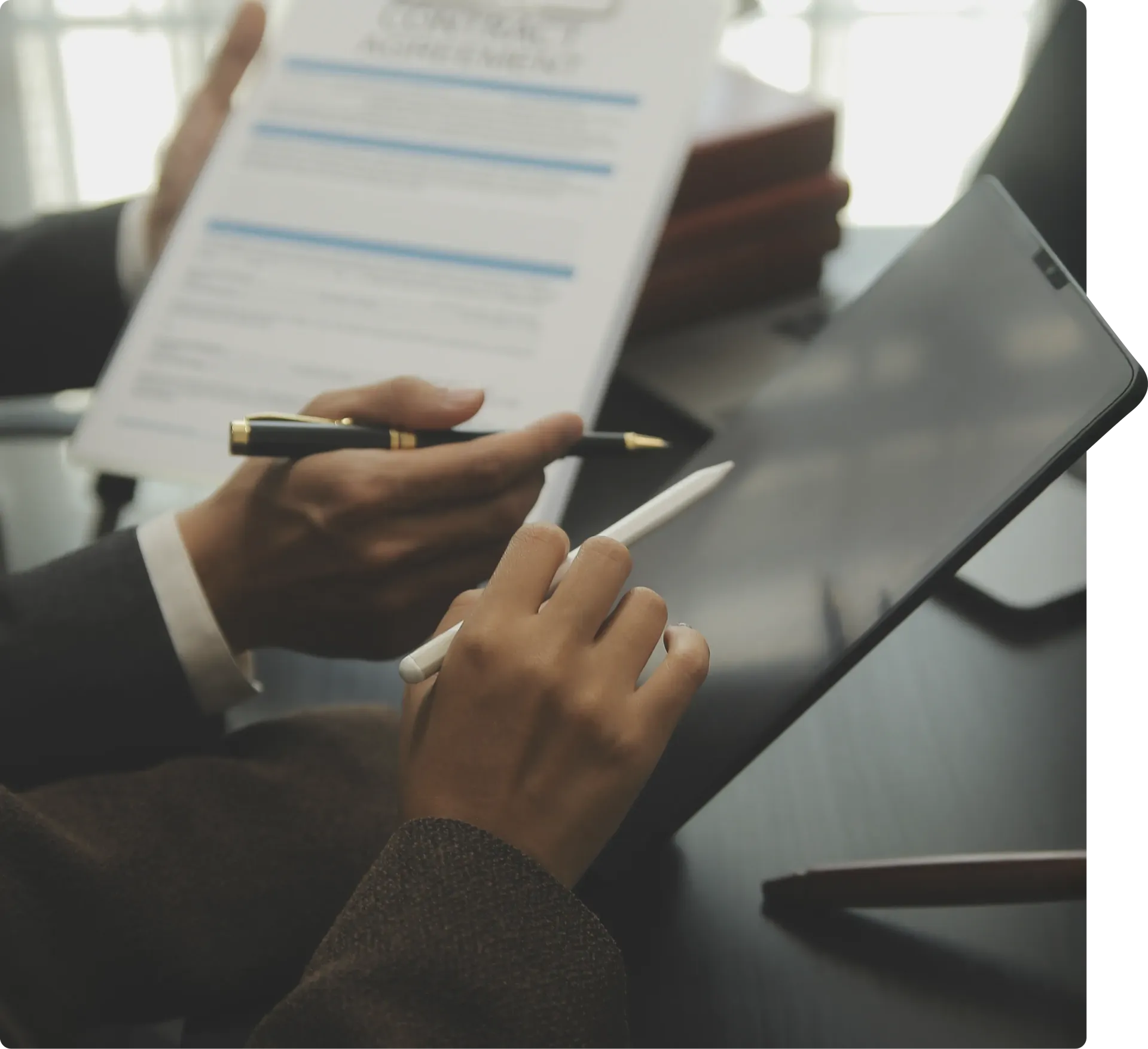 Mãos apontando para um documento e um tablet. Uma caneta é usada no tablet, assinando um contrato.