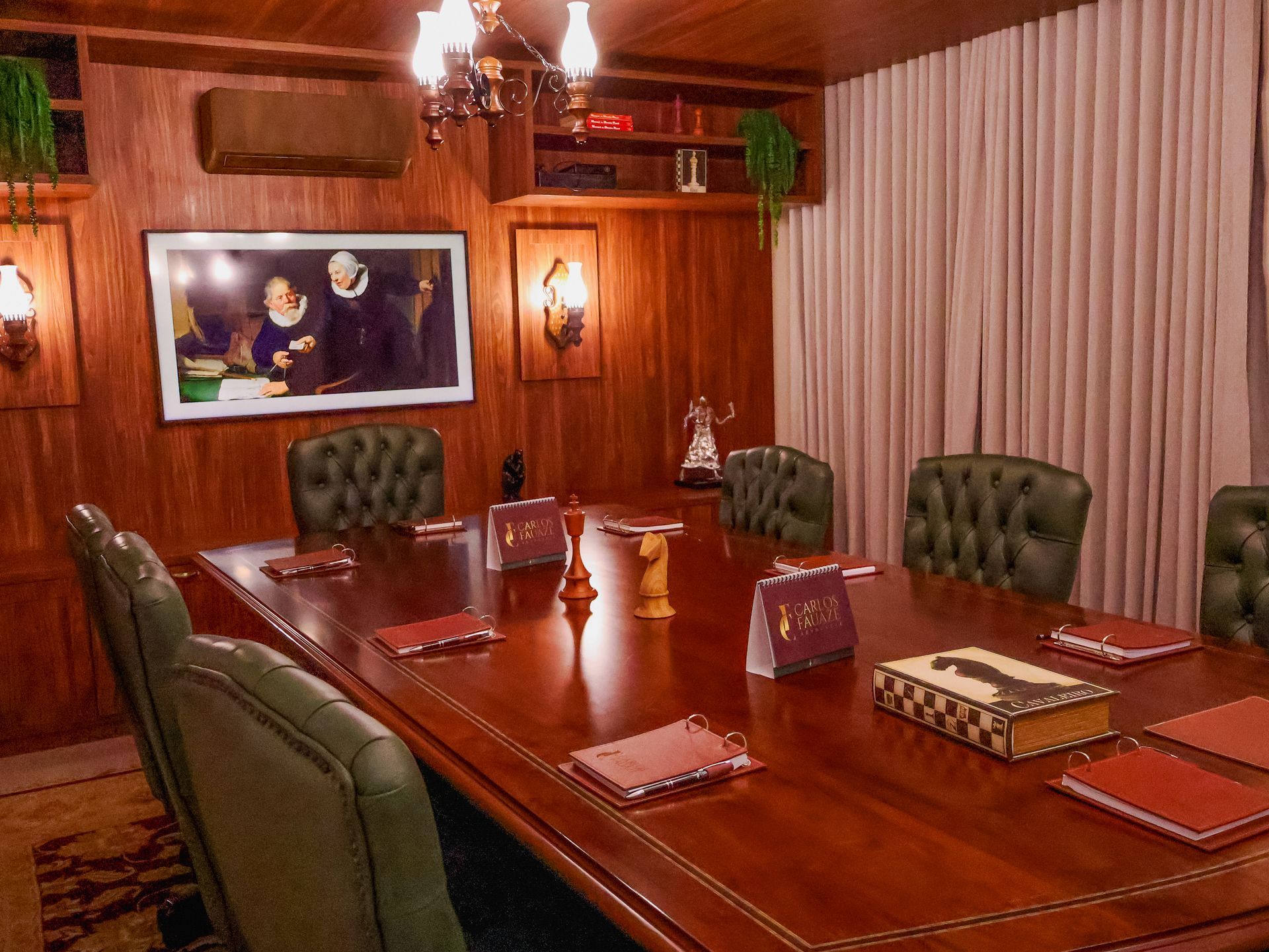 Uma sala de reuniões clássica com painéis de madeira, uma mesa grande, cadeiras verdes estofadas e um retrato na parede.