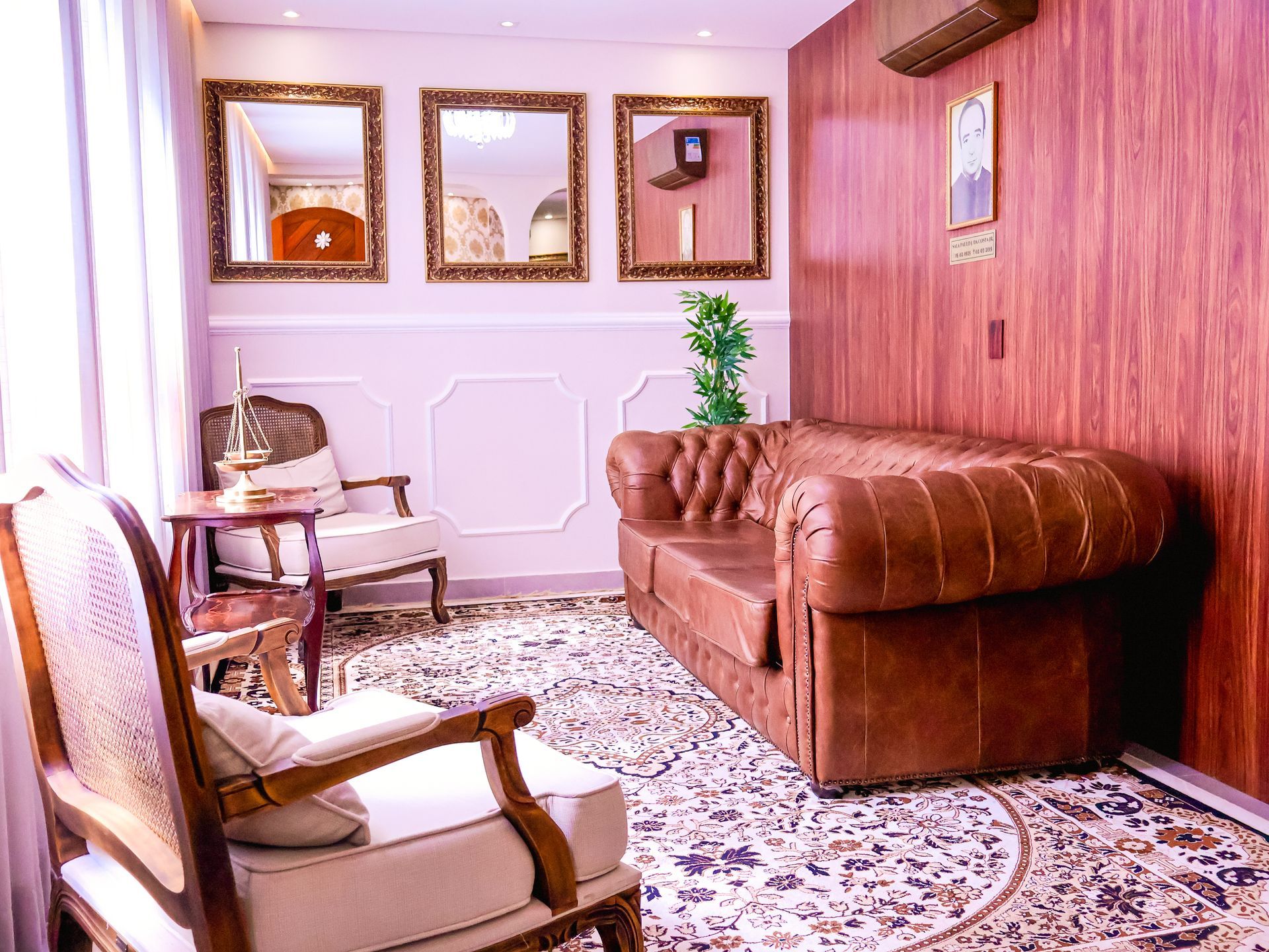 Sala elegante com sofá de couro, cadeiras ornamentadas, espelhos antigos e painéis de madeira.