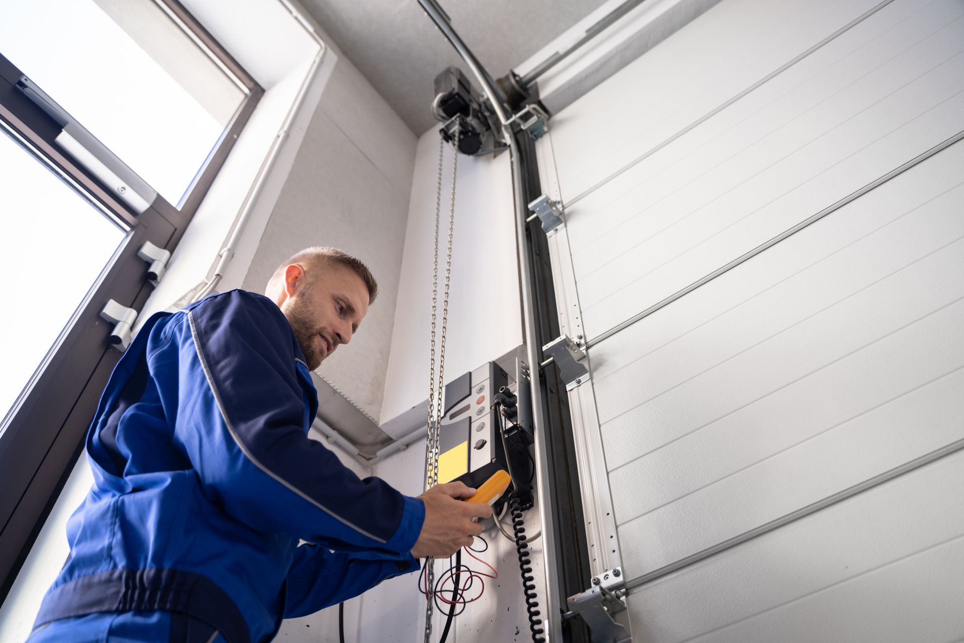 Technician in blue uniform testing garage door opener with multimeter.