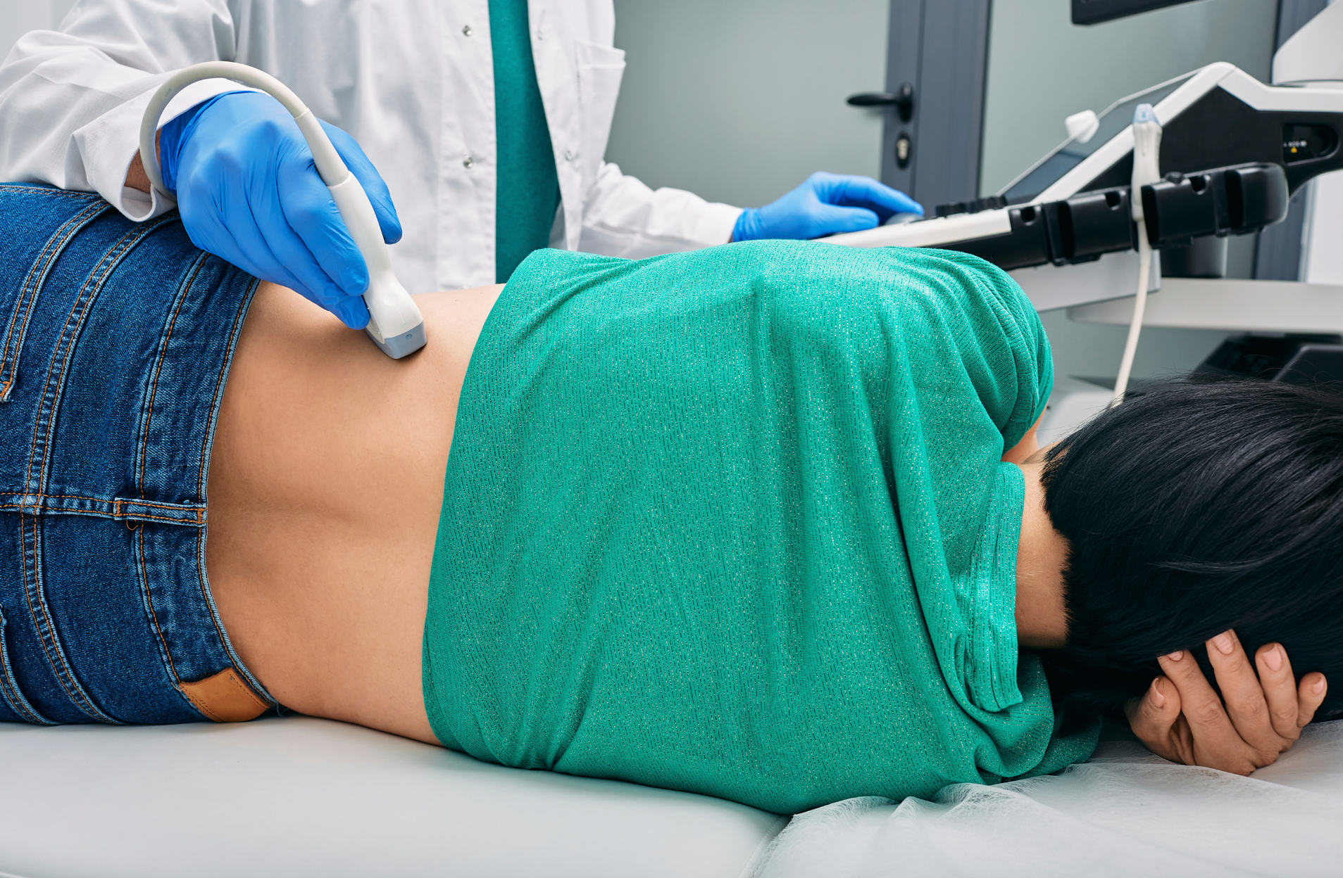 A woman is laying on a bed getting an ultrasound on her back.