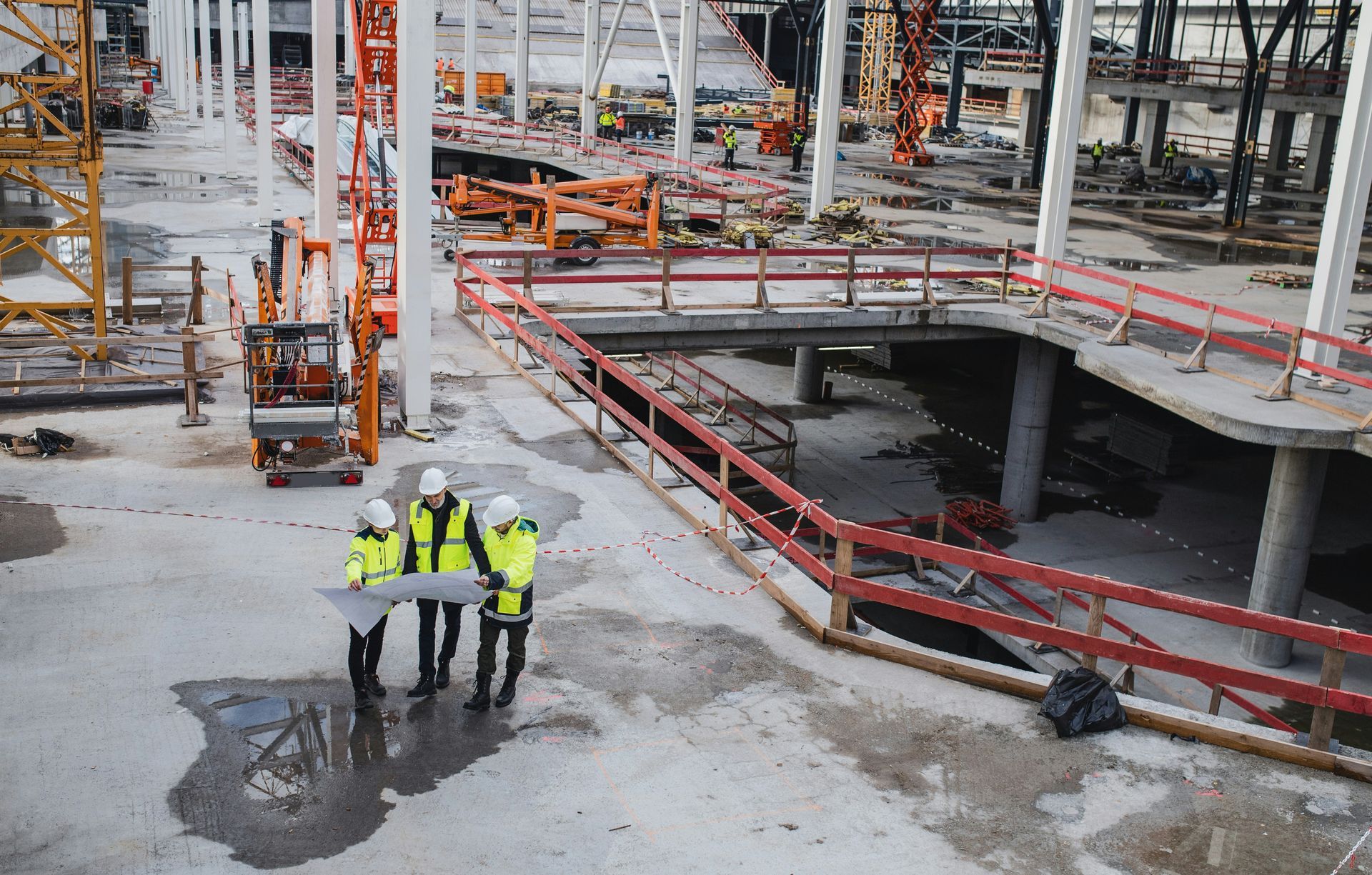 Construction workers in safety vests and hard hats reviewing blueprints on a construction site.