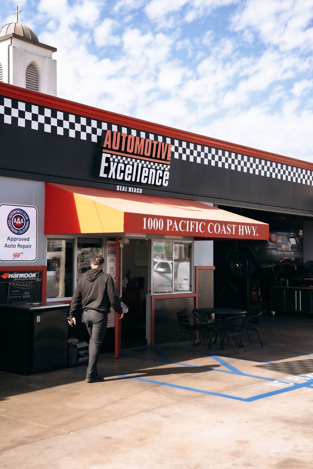 A man is walking in front of an auto body shop.